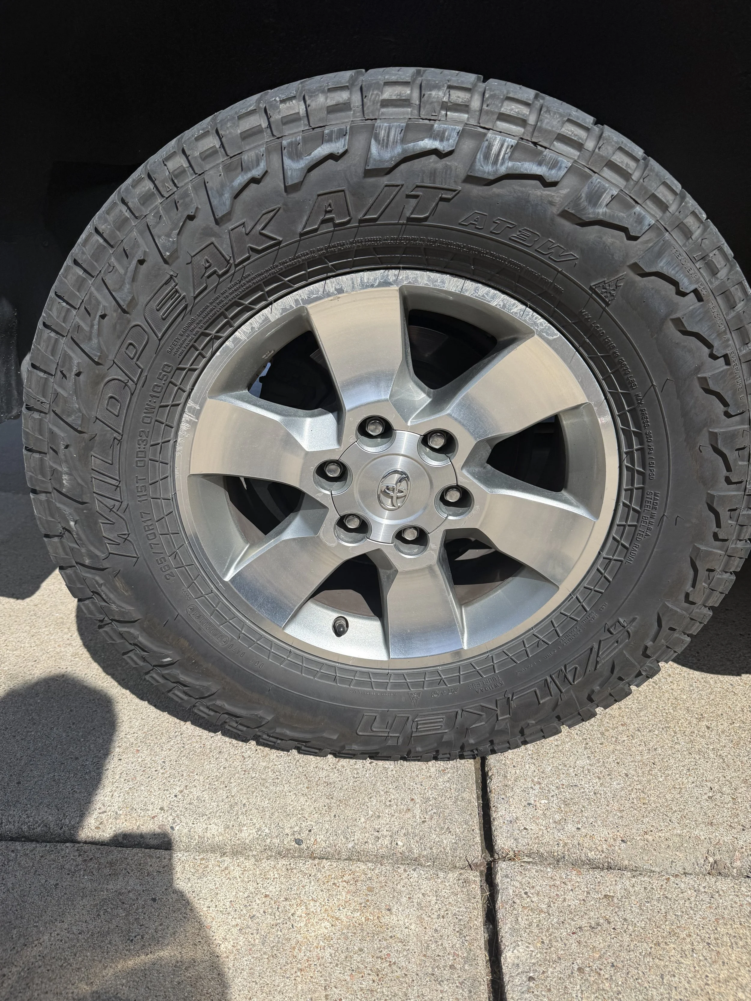 A close-up of a vehicle's tire with a rim, placed on a concrete sidewalk.