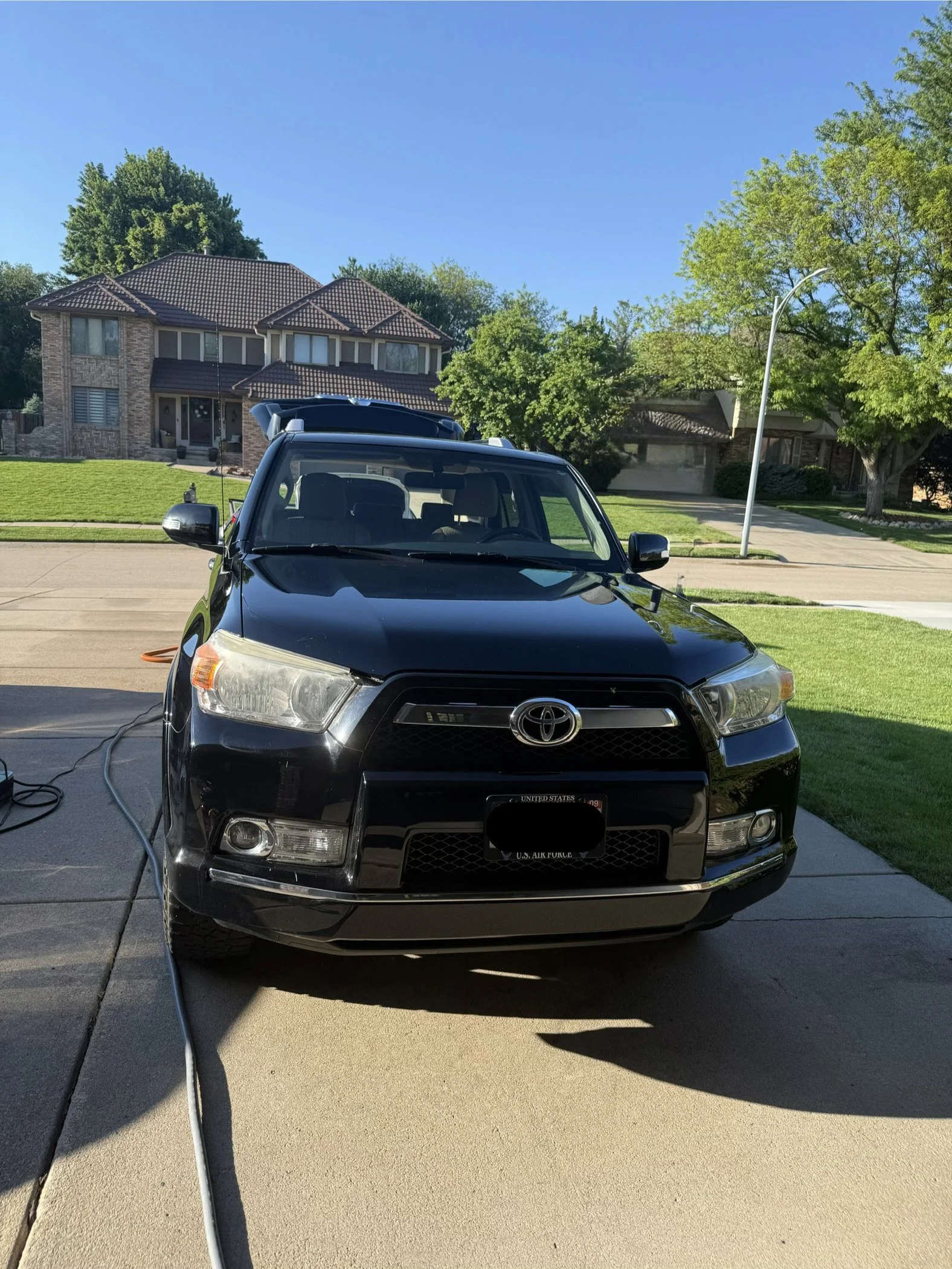 Black Toyota car parked on a driveway in front of a house, with a lawn and trees, and a blue sky above.