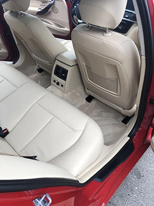 Interior of a car's back seat area with beige leather seats, center console with controls, and air vents.