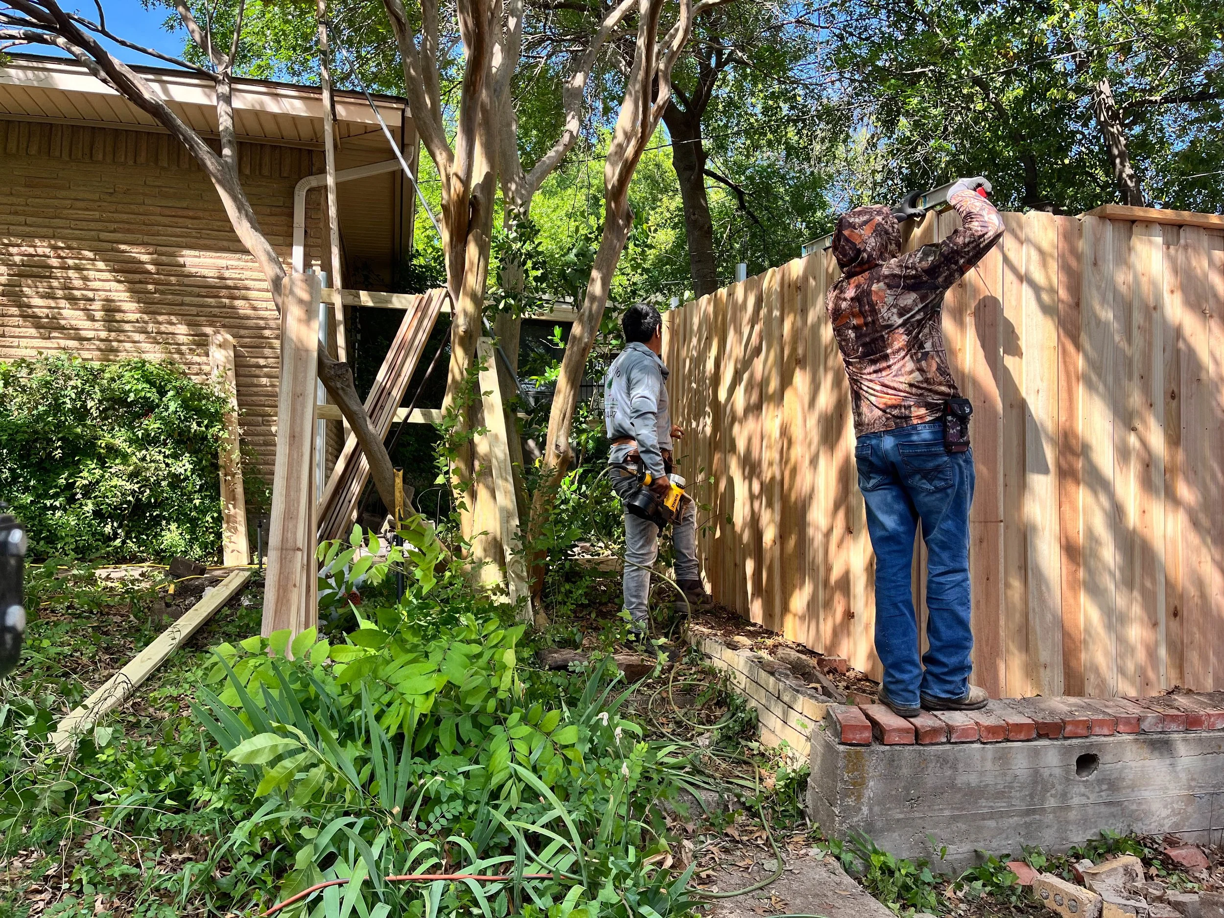 Romero Tree Service working together building a wooden fence in a garden.