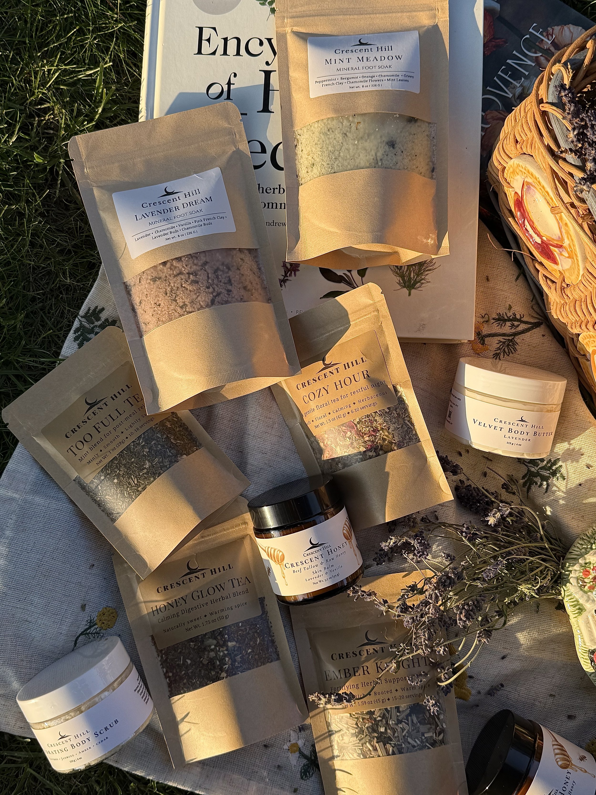 Assorted Crescent Hill brand herbal and natural wellness products such as foot soaks, body scrubs, and body butter on a table with greenery.