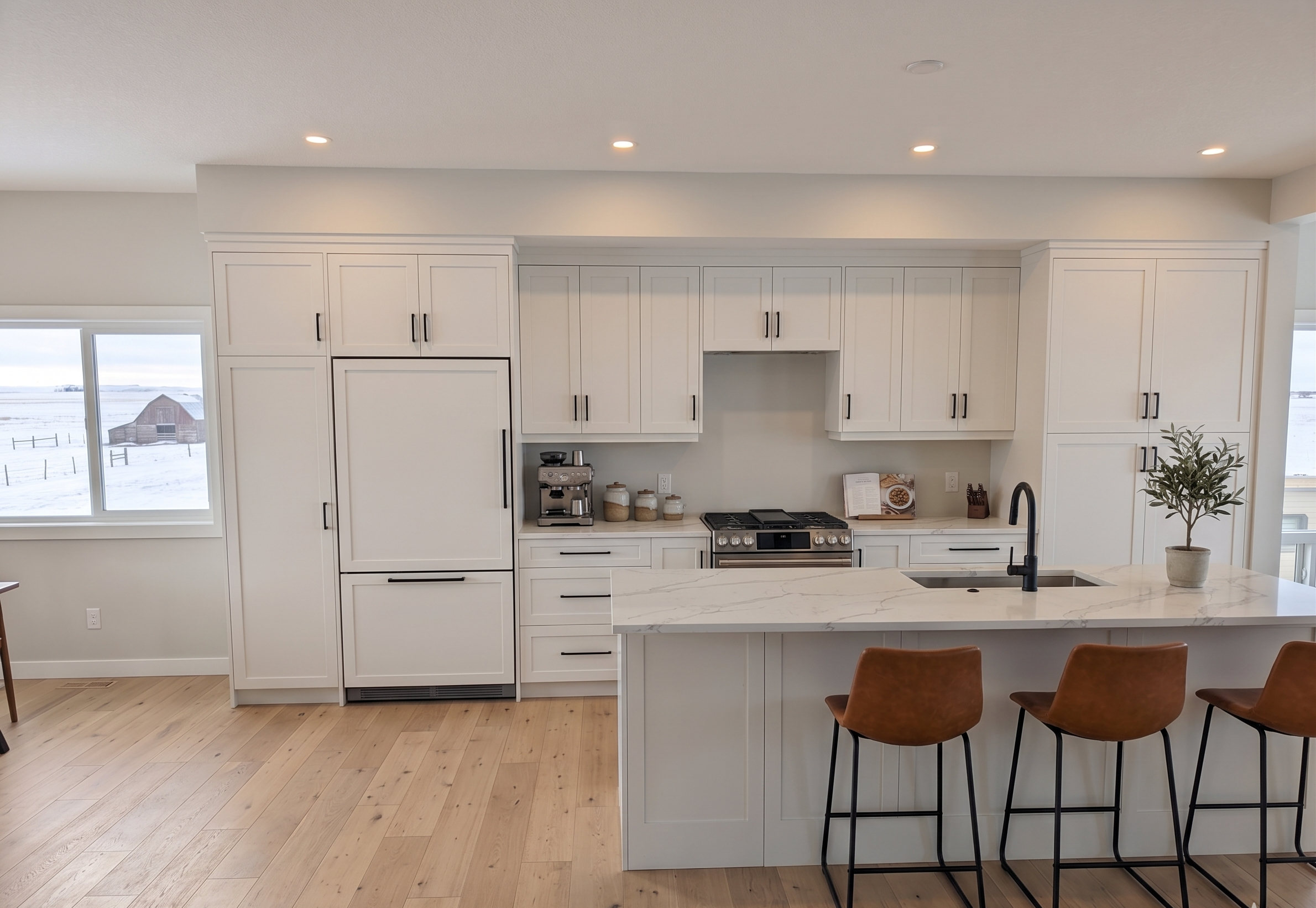 Modern kitchen with white cabinets, a marble island, stainless steel appliances, light wood flooring, and a view of a snowy landscape with a barn outside the window.