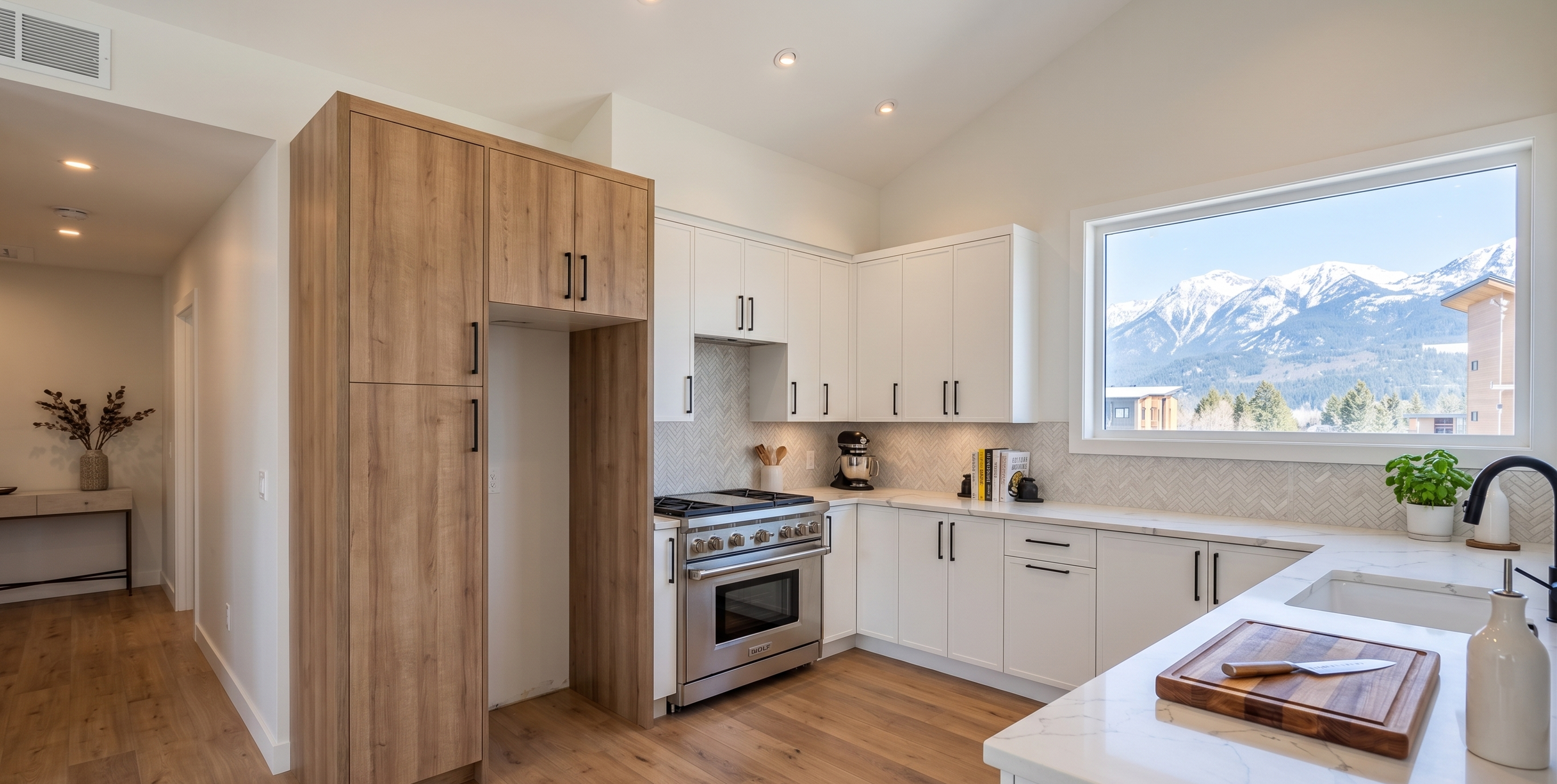 Modern kitchen with white cabinets, a large window overlooking snowy mountains, a stainless steel oven, black faucet, and a potted plant on the countertop.