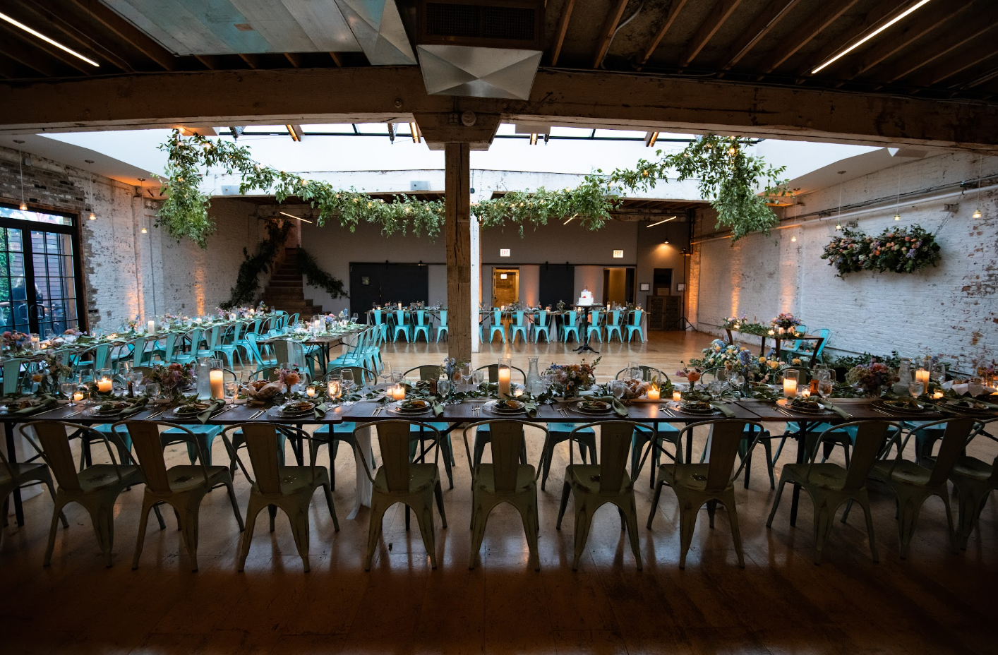 image of the joinery wedding venue, with skylight and lots of natural lights, hanging floral and greenery from the string lights, natural wood tables and blue chairs