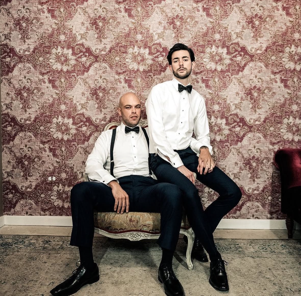 image of two grooms in a wedding suite with a fun pink wallpaper and vintage furniture at the joinery