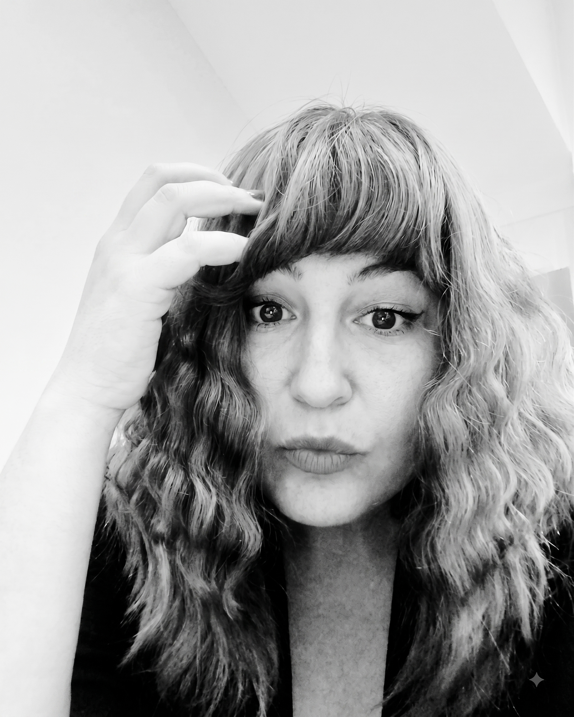 A woman with curly hair and large eyes is touching her forehead with her right hand, looking directly at the camera, wearing a furry collar.
