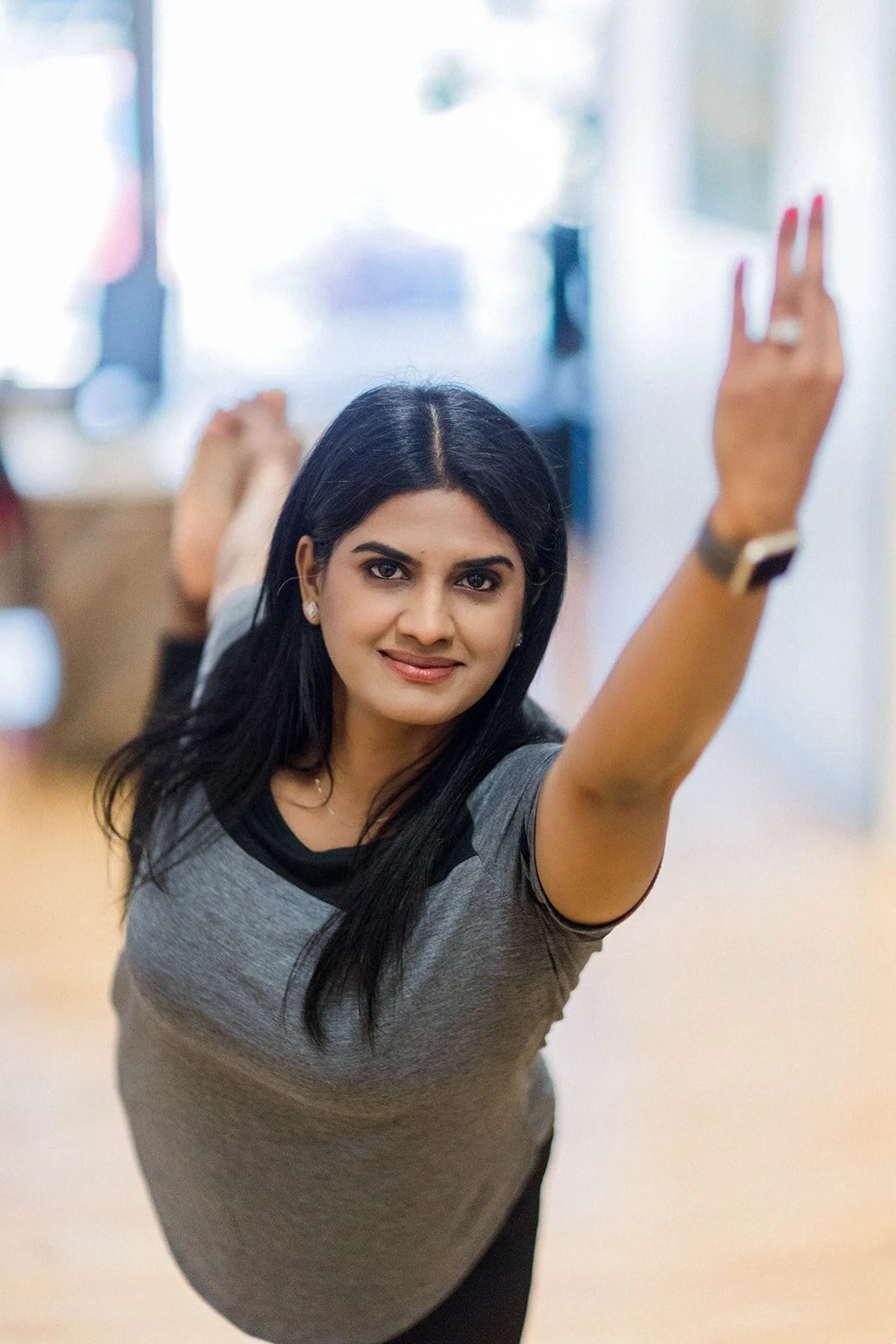 Woman practicing yoga or stretching indoors, lying on her stomach with one arm raised and hand making a peace sign.