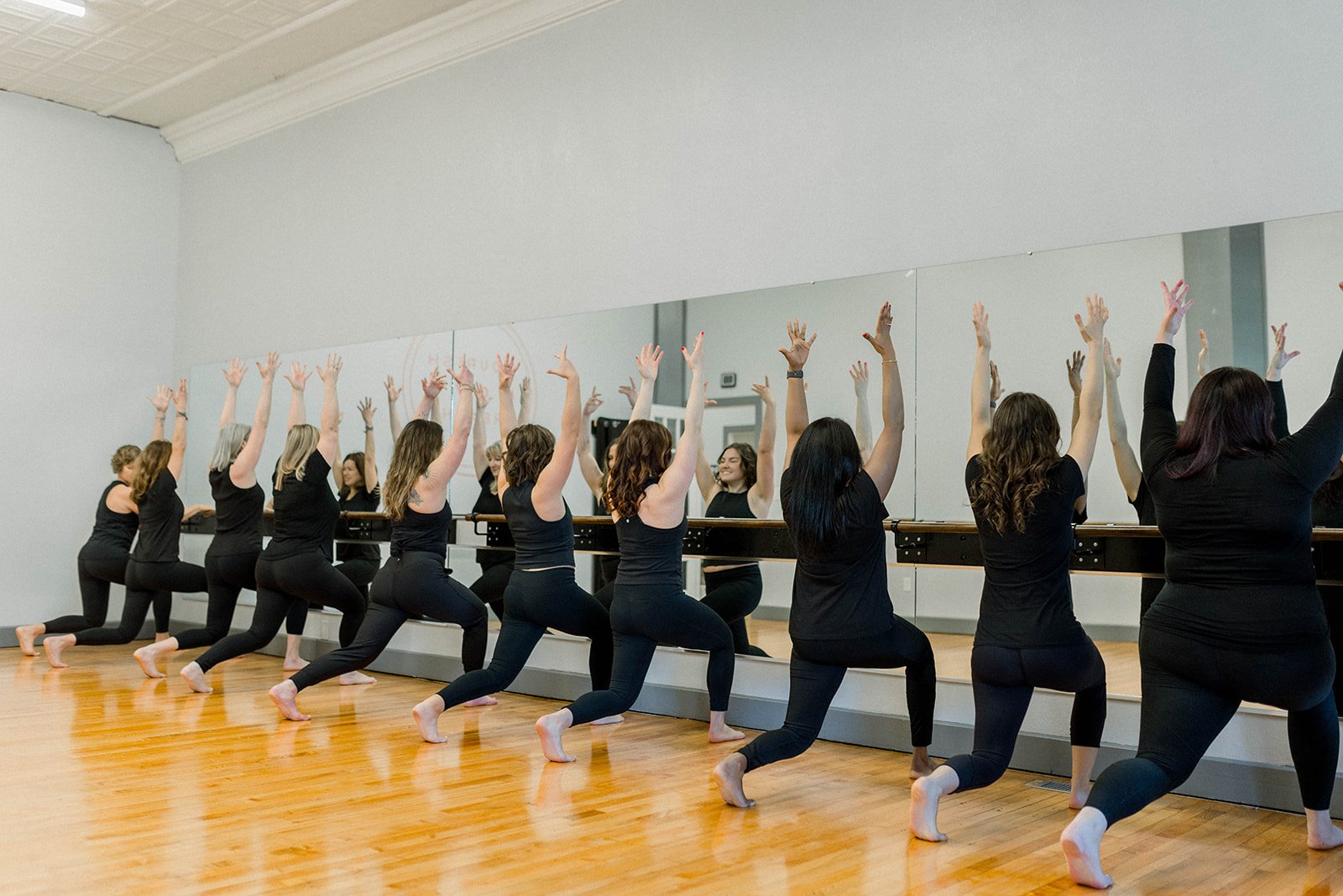 Group of women in black clothing practicing yoga in front of mirrors in a dance studio.