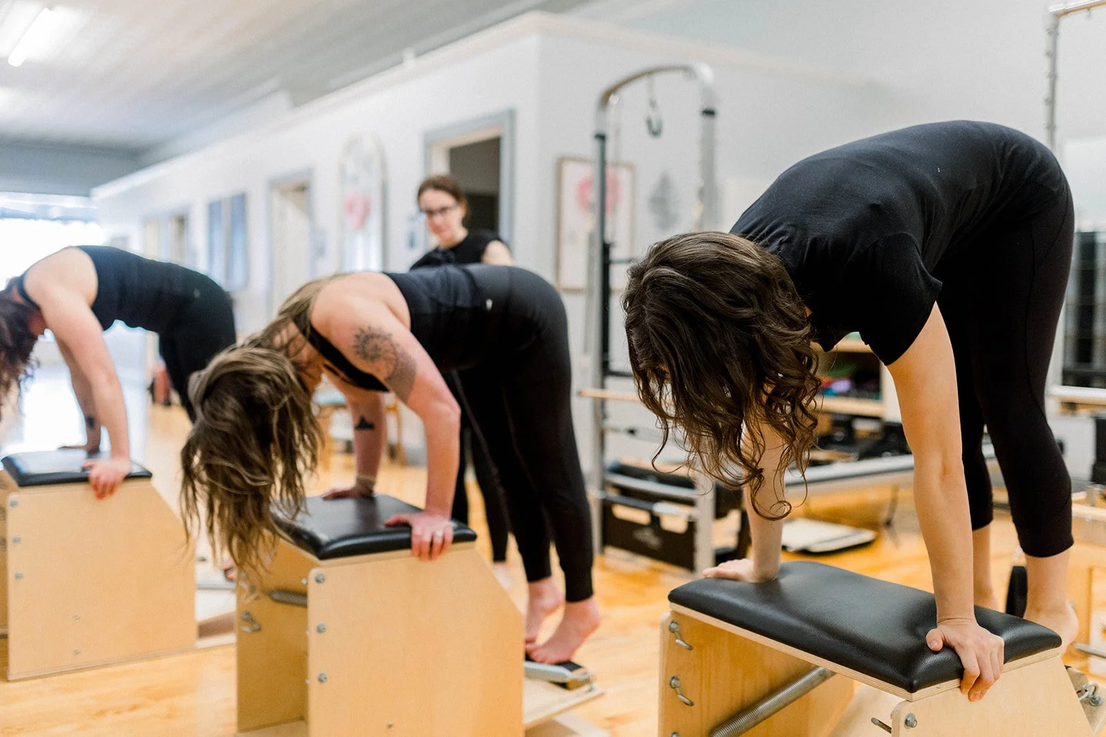 Women practicing yoga in a studio, bending forward with hands on yoga benches.