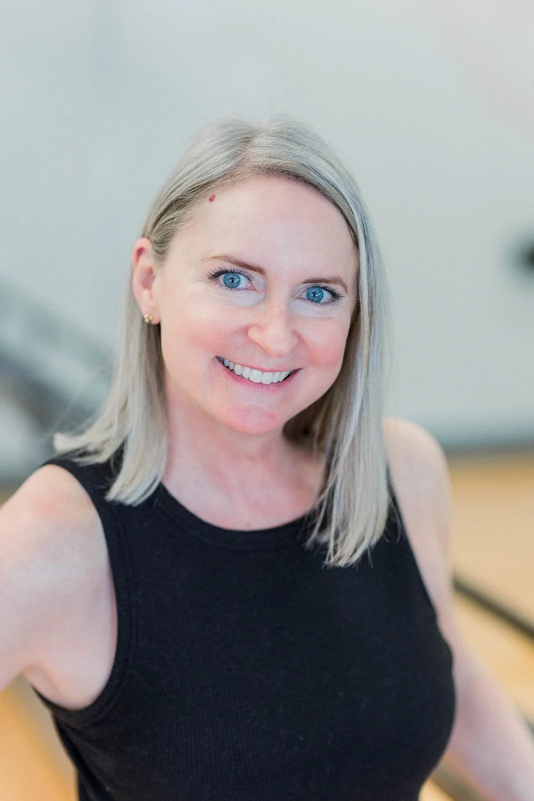 A woman with shoulder-length blonde hair and blue eyes smiling, wearing a black sleeveless top.