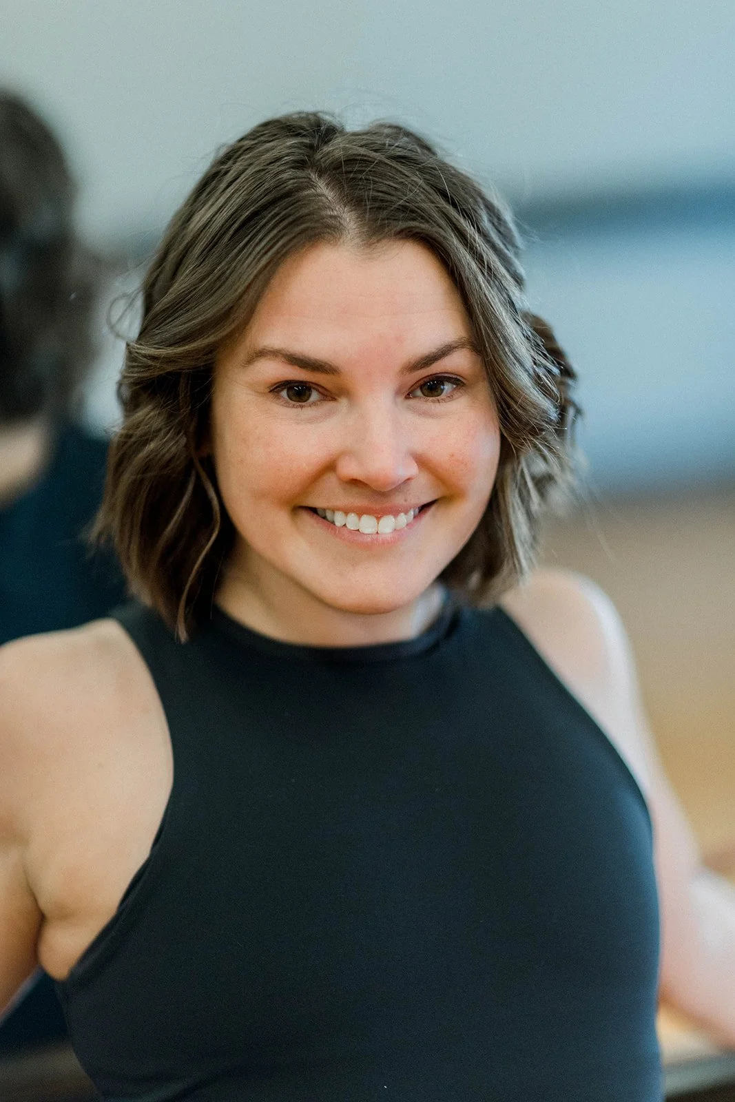 A woman with shoulder-length brown hair smiling, wearing a black sleeveless top.