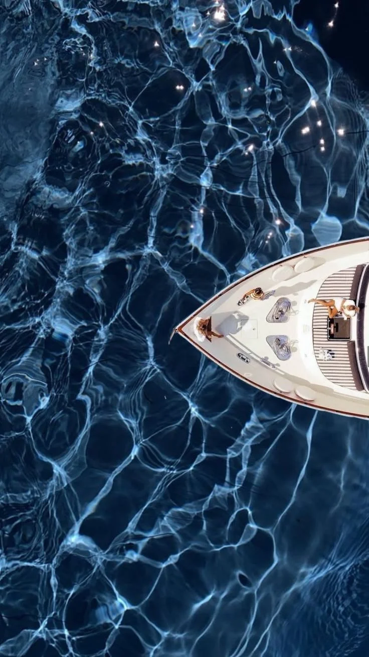 Top-down view of a boat floating on deep blue water with sunlight reflections.