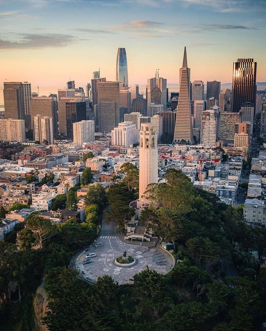 San Francisco skyline at sunset featuring Coit Tower in the foreground and various high-rise buildings in the downtown area.