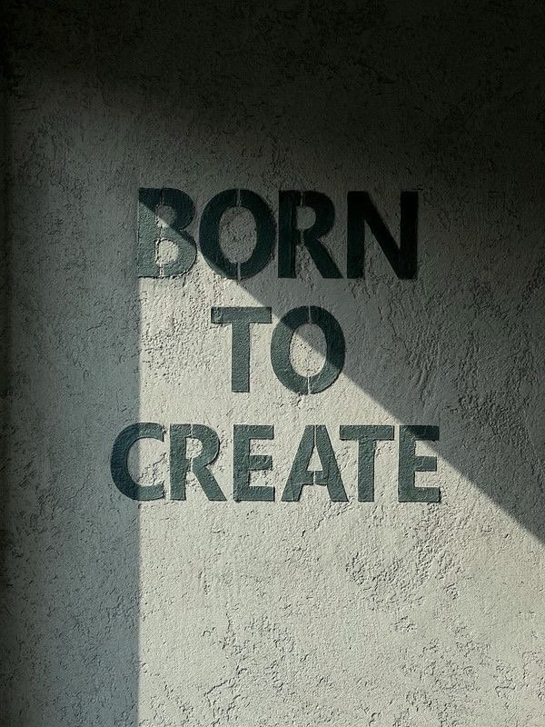 Wall with the phrase 'Born to Create' painted on it, with a shadow cast across the words.