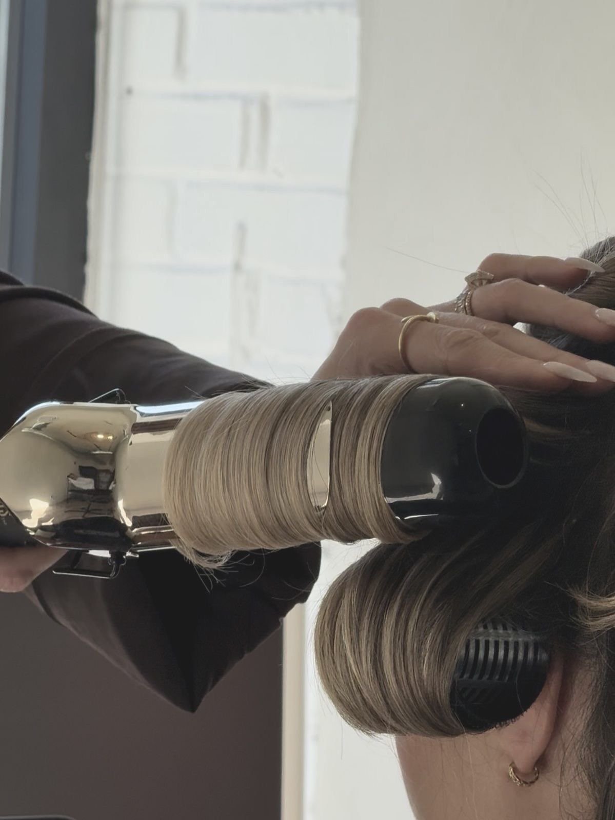 Hairdresser applying blonde highlights or hair dye to a woman's hair with a hairbrush and spray bottle, using a professional hair care technique.
