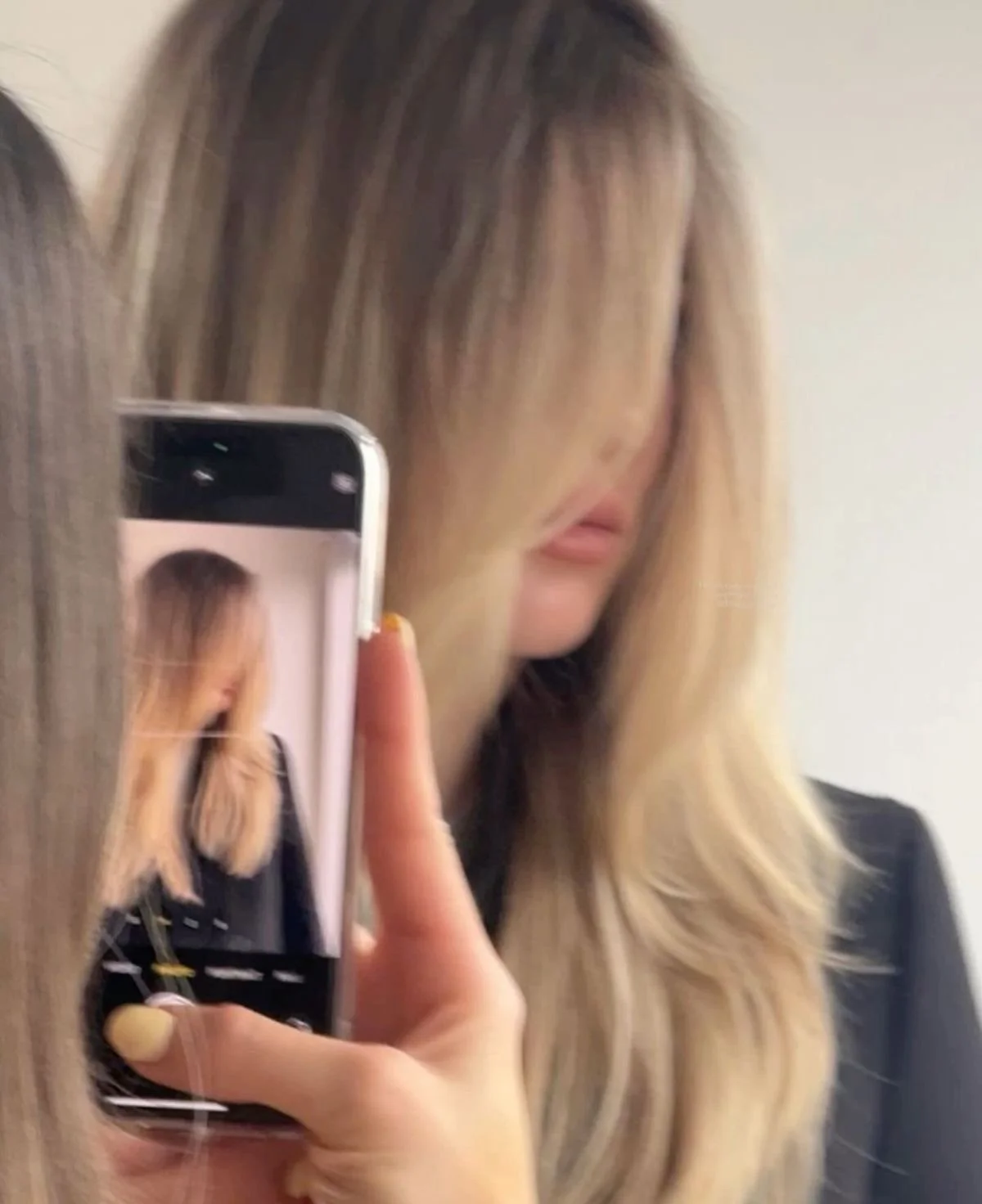 A woman taking a mirror selfie with her smartphone, focusing on her long, blonde hair and lips, partially obscuring her face.