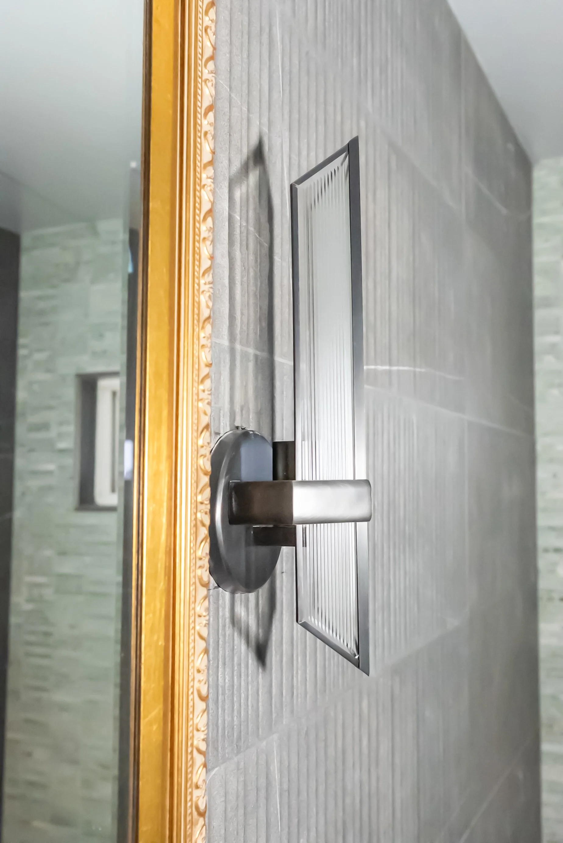 A black door handle with a security lock on a metal door set into gray tiled wall.