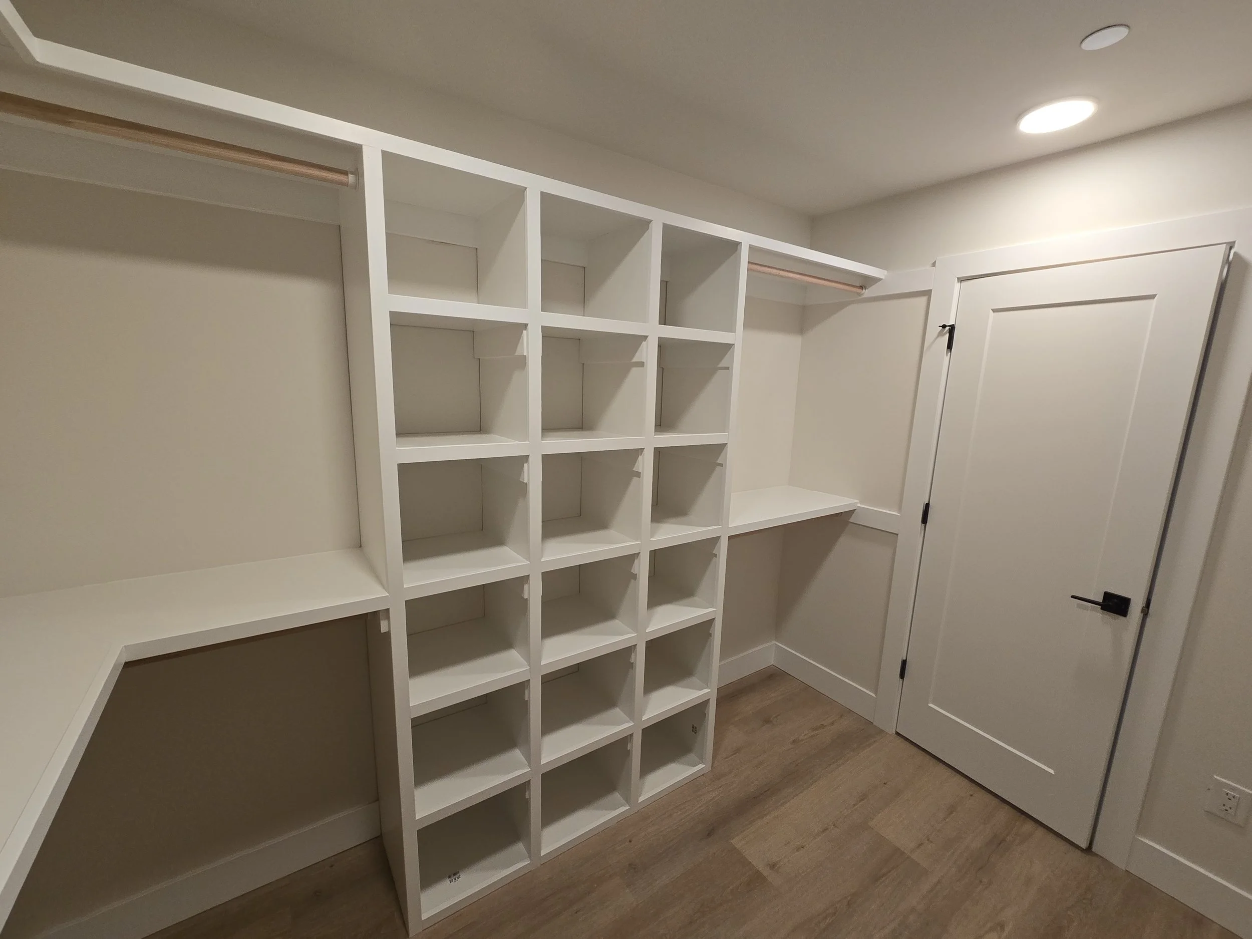 Empty white built-in shelving unit with cubbies and hanging rods in a small room