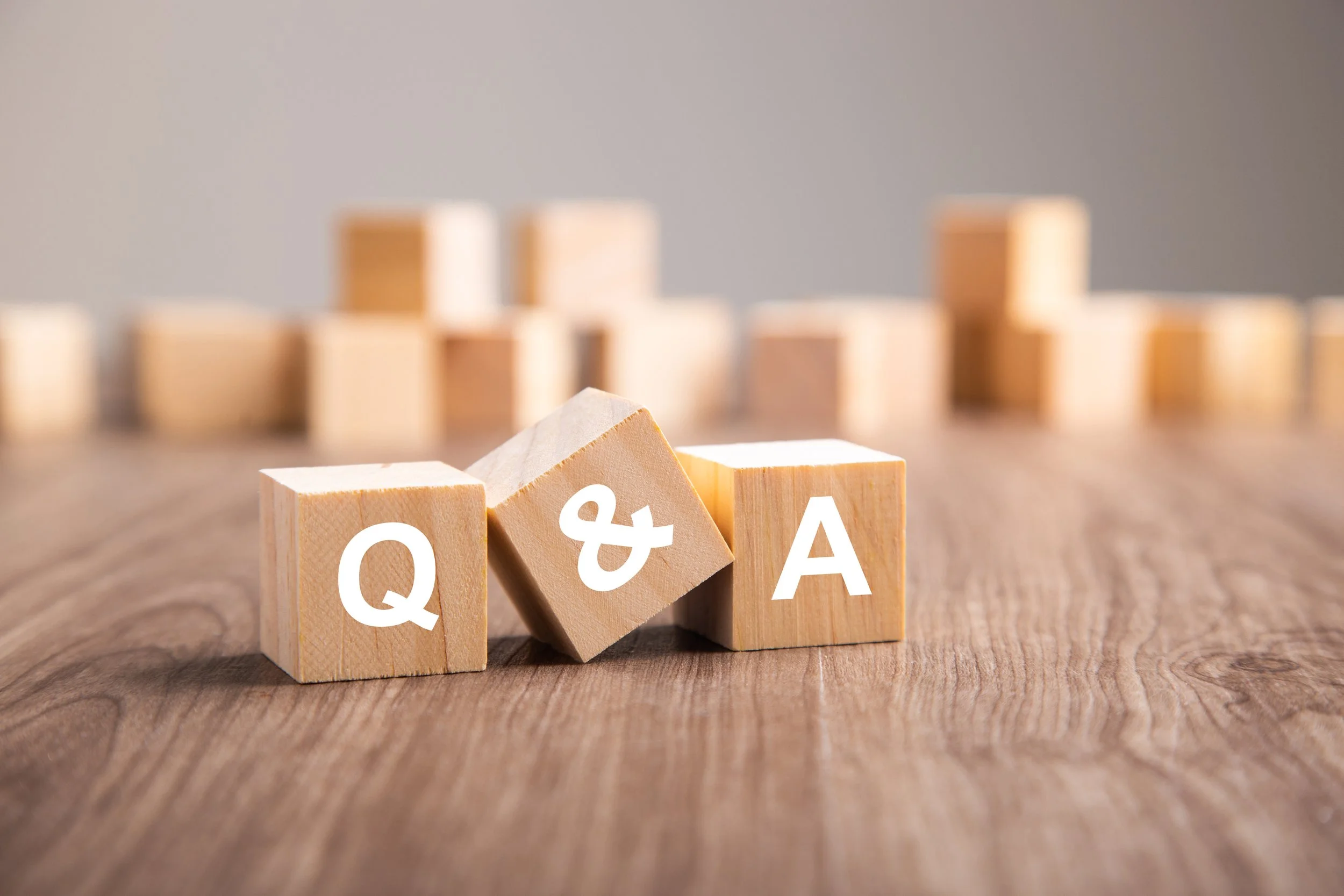 Wooden blocks with white letters spelling 'Q & A' on a wooden surface, with other blocks blurred in the background.