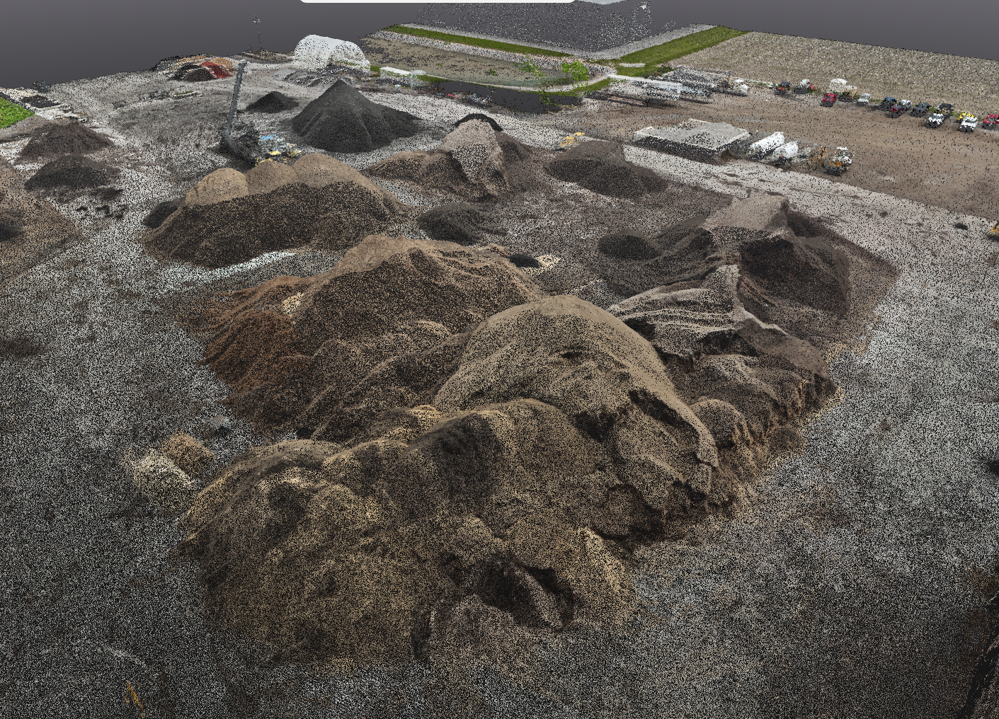 Large excavated dirt piles and construction site with vehicles and infrastructure in the background.