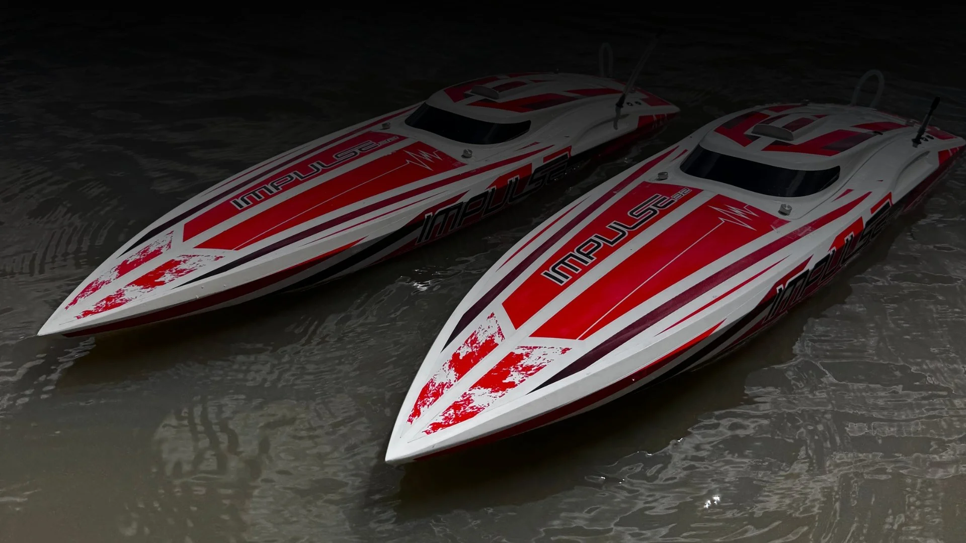 Two remote-controlled race boats floating on water with red, white, and black designs.
