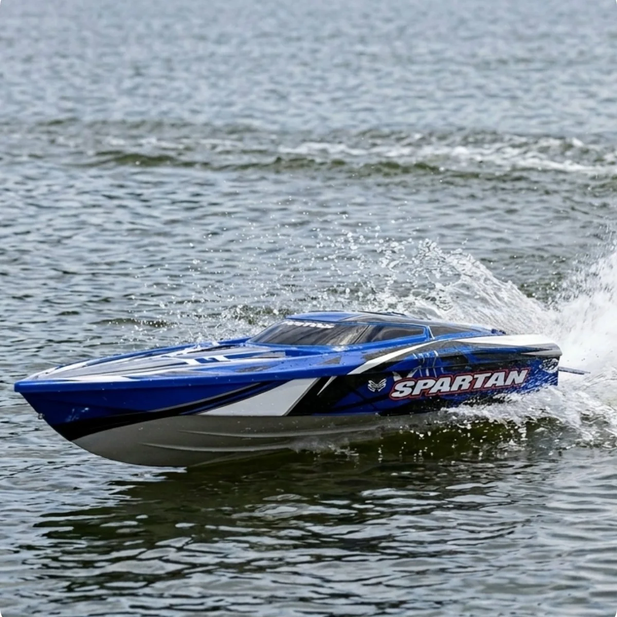 A blue and white remote-controlled speedboat named Spartan moving quickly on water, creating a wake behind it.