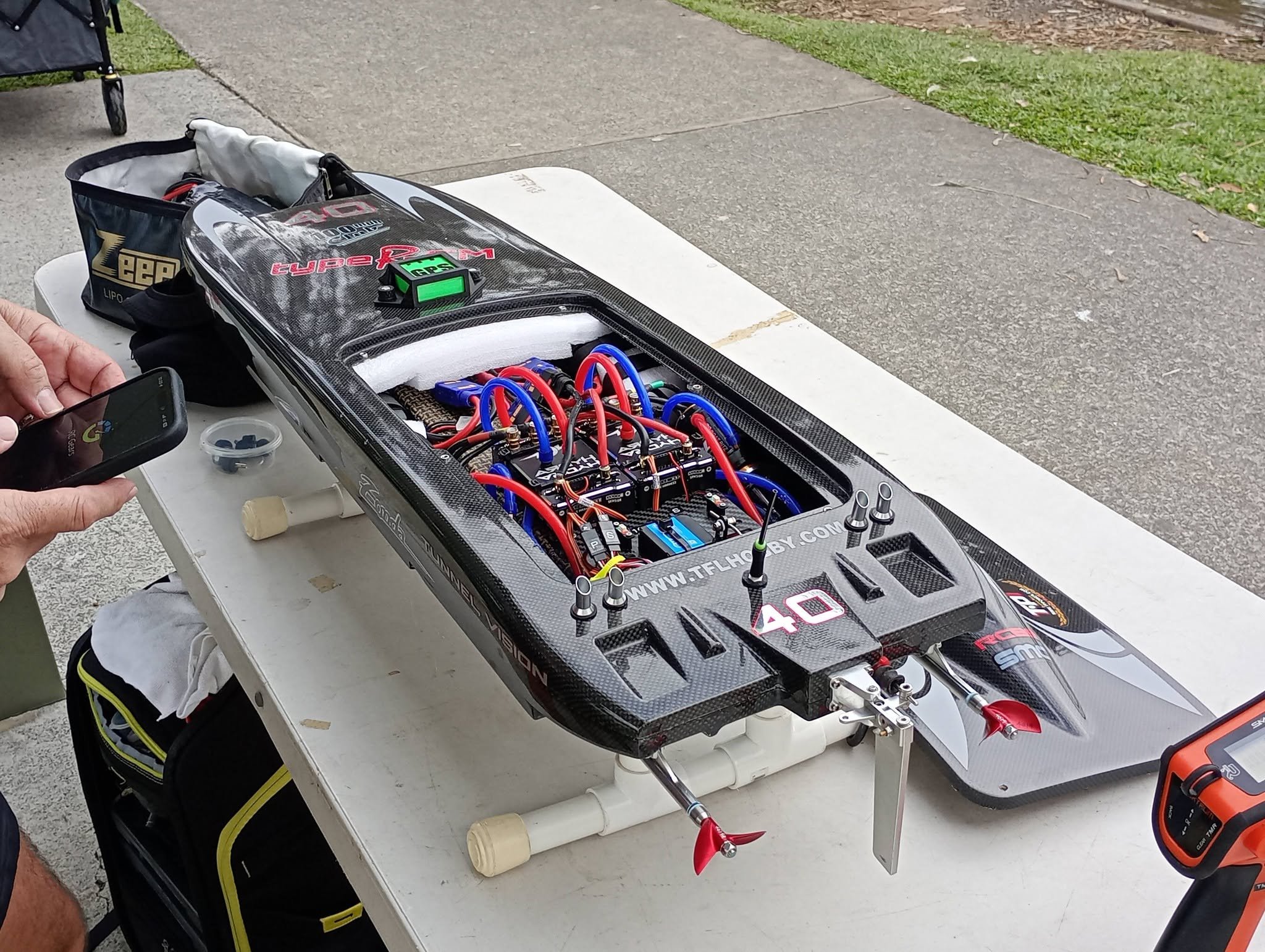 A close-up of a remote-controlled race car with various electronic components and wiring, placed on a white table outdoors.
