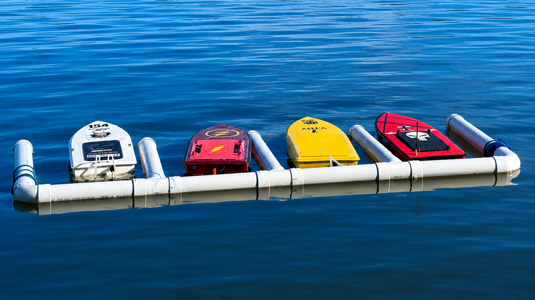 Four small boats with colorful hulls anchored on a floating platform in calm water.
