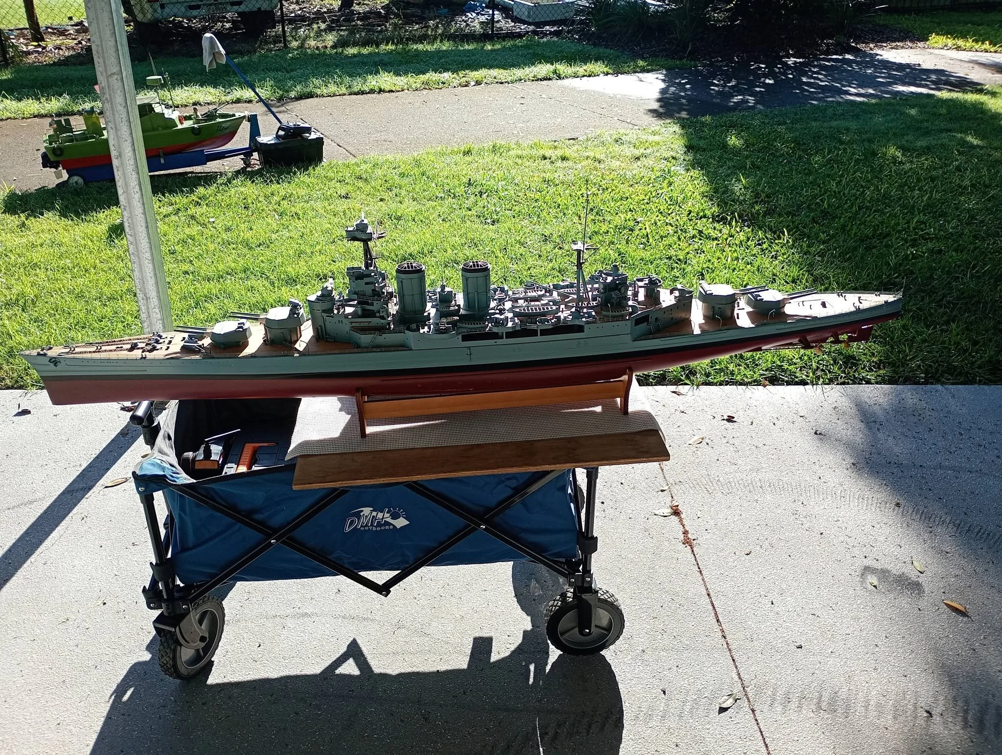 A model battleship placed on a stand outside on a patio, with a grassy yard and a sidewalk in the background.
