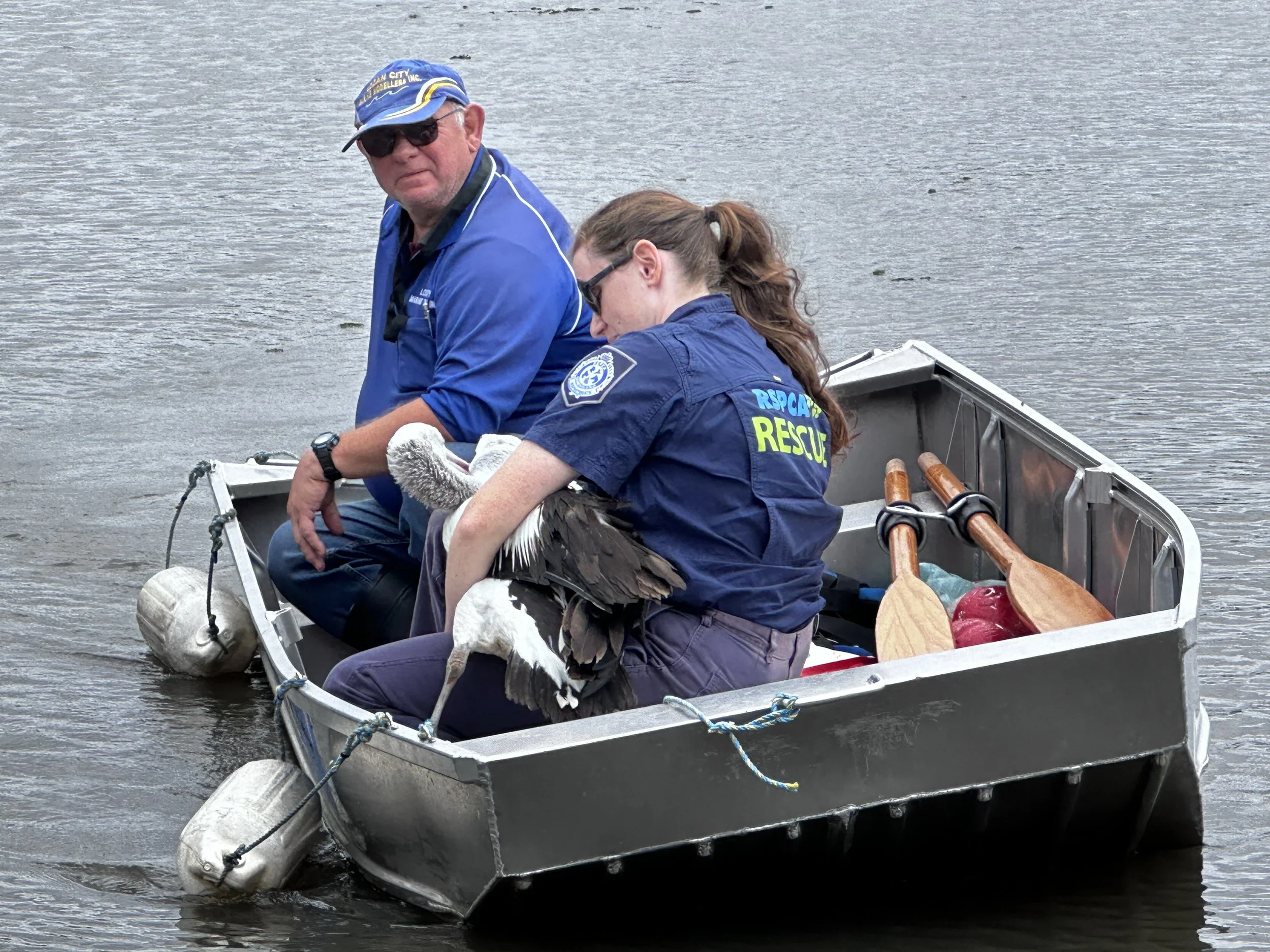 Two rescue workers in a boat on a body of water with an inflatable and paddles, one holding a duck, during a rescue operation.