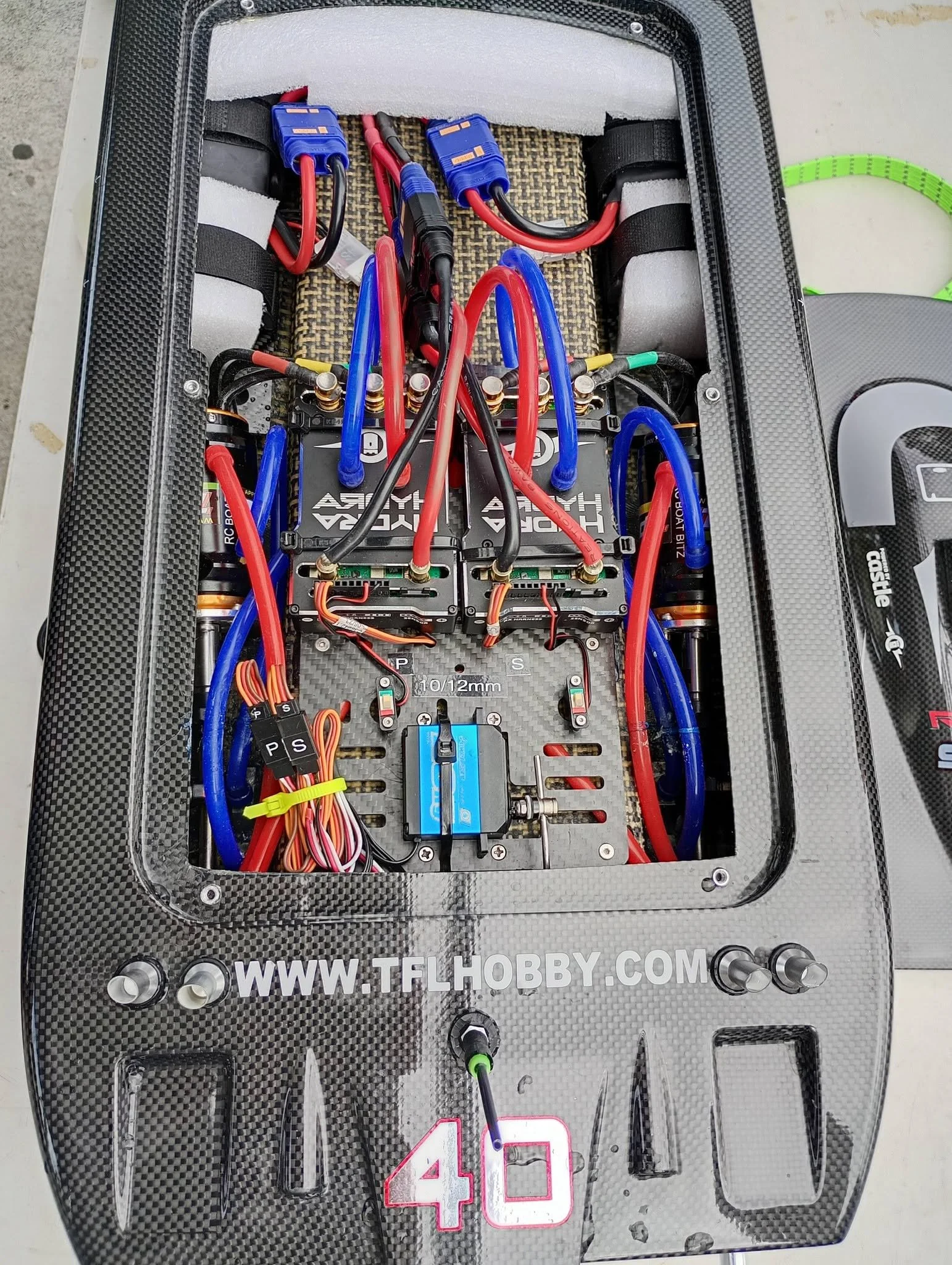 Close-up of a race car cockpit with exposed electronics and wiring, including two batteries labeled 'HYPER' and a number 40 on the dashboard.