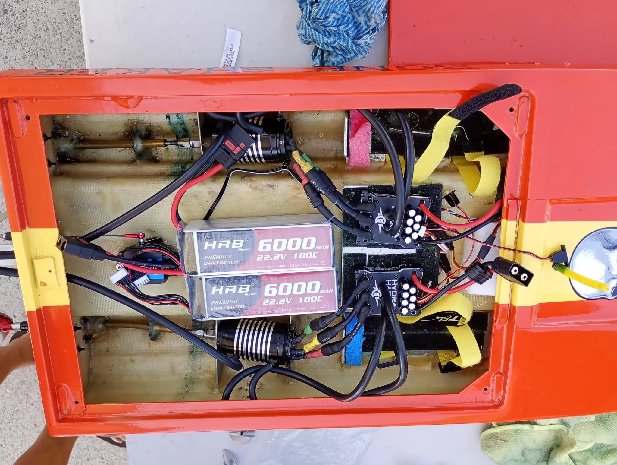 An open orange remote-controlled car with visible internal electrical components, including batteries, wires, and motors, placed on a flat surface.