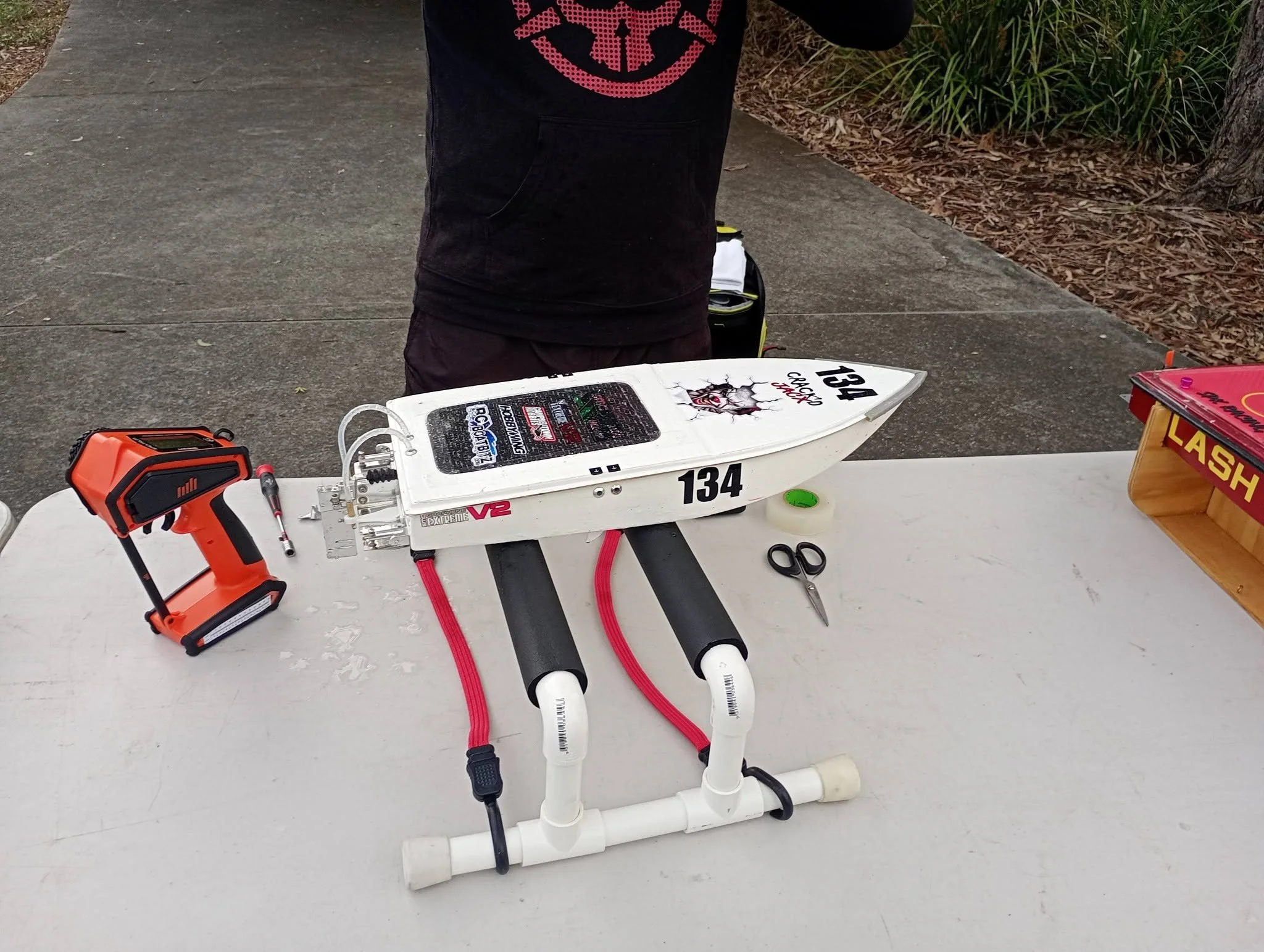 A remote-controlled boat on a table with tools nearby, outdoors on a paved surface.