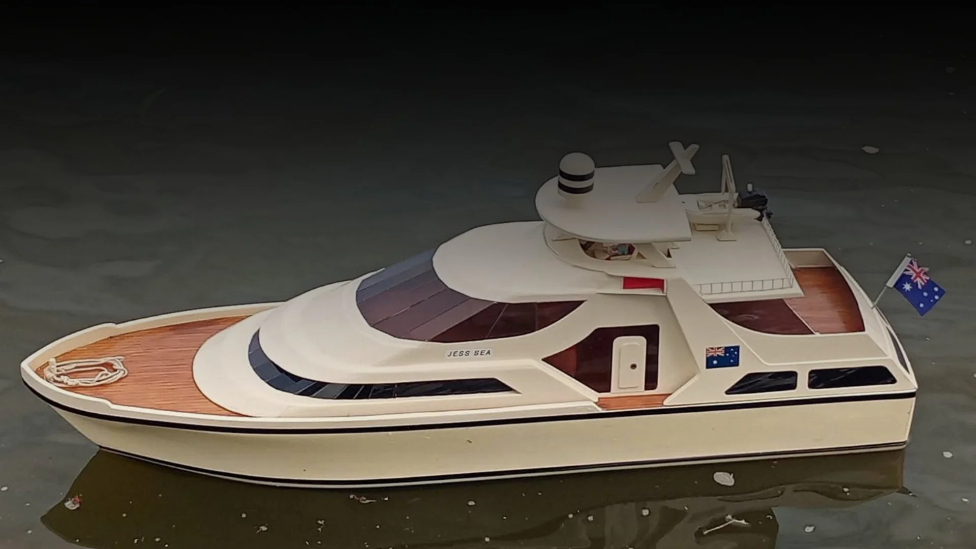 A luxury white yacht named Jess Sea with Australian flags, floating on water, featuring wooden decks, multiple levels, and modern design elements.