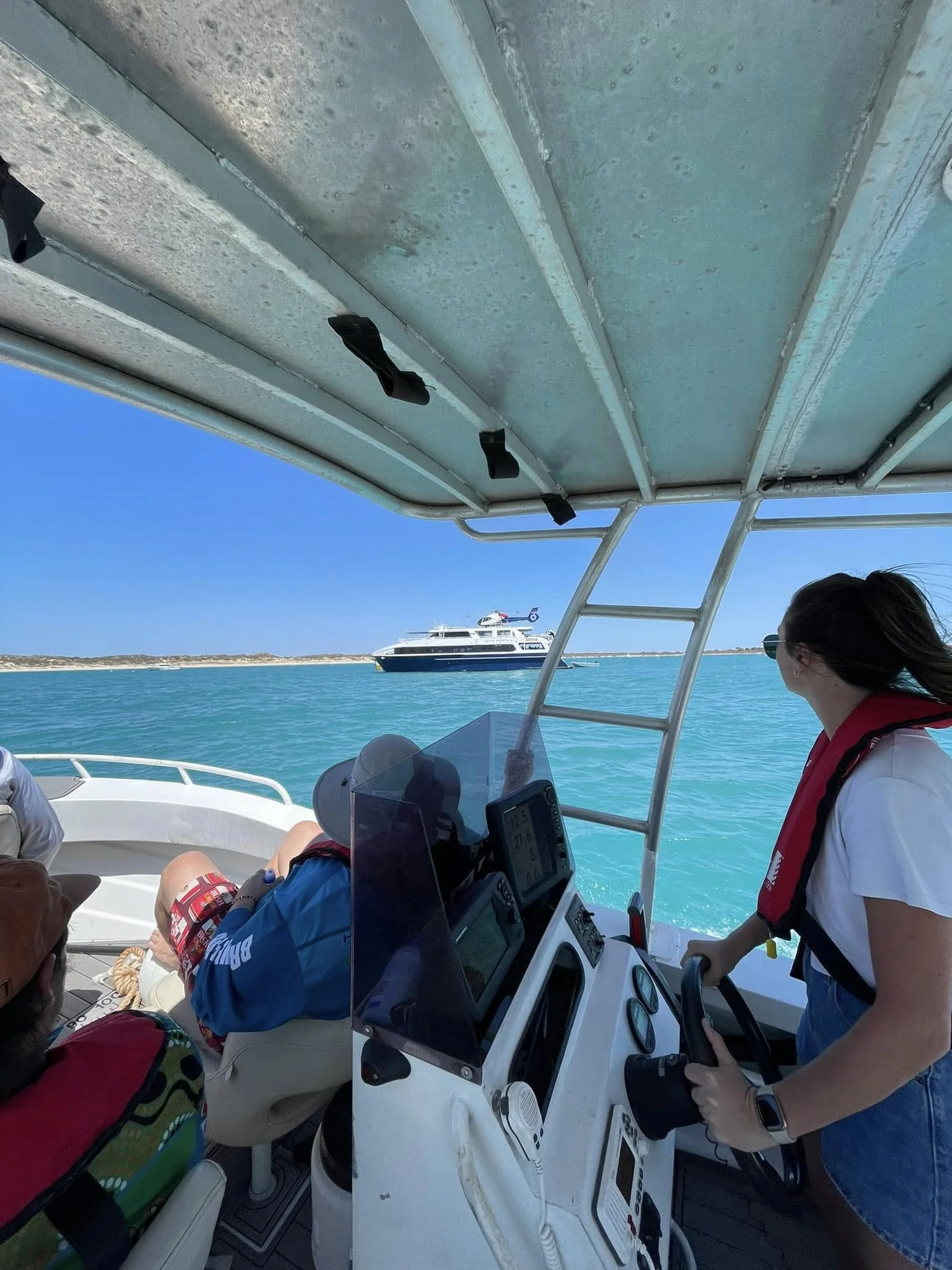 People on a boat with a large luxury yacht in the background in open water under a clear blue sky.