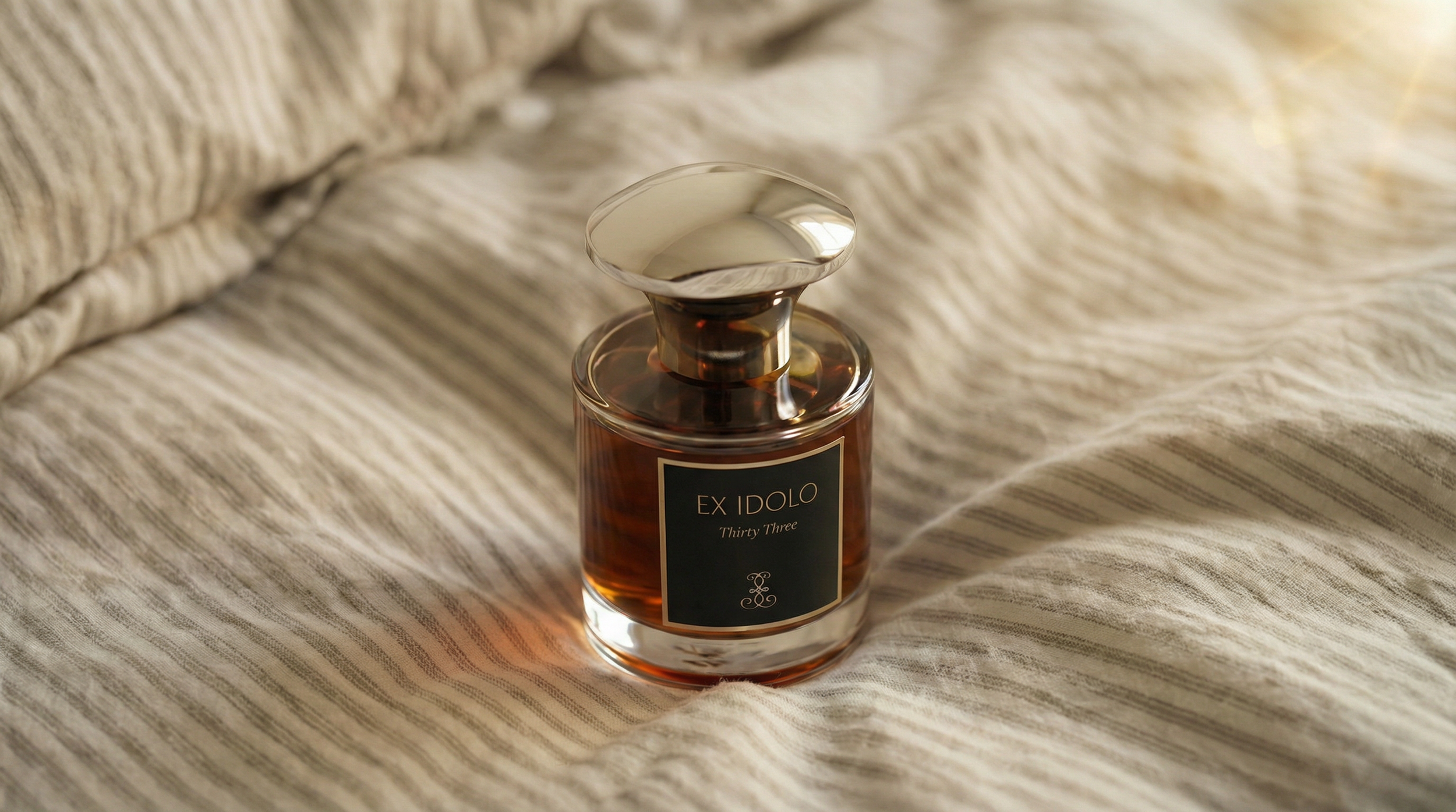 A perfume bottle labeled 'EX IDOLO Thirty Three' placed on a textured, light-colored fabric surface.