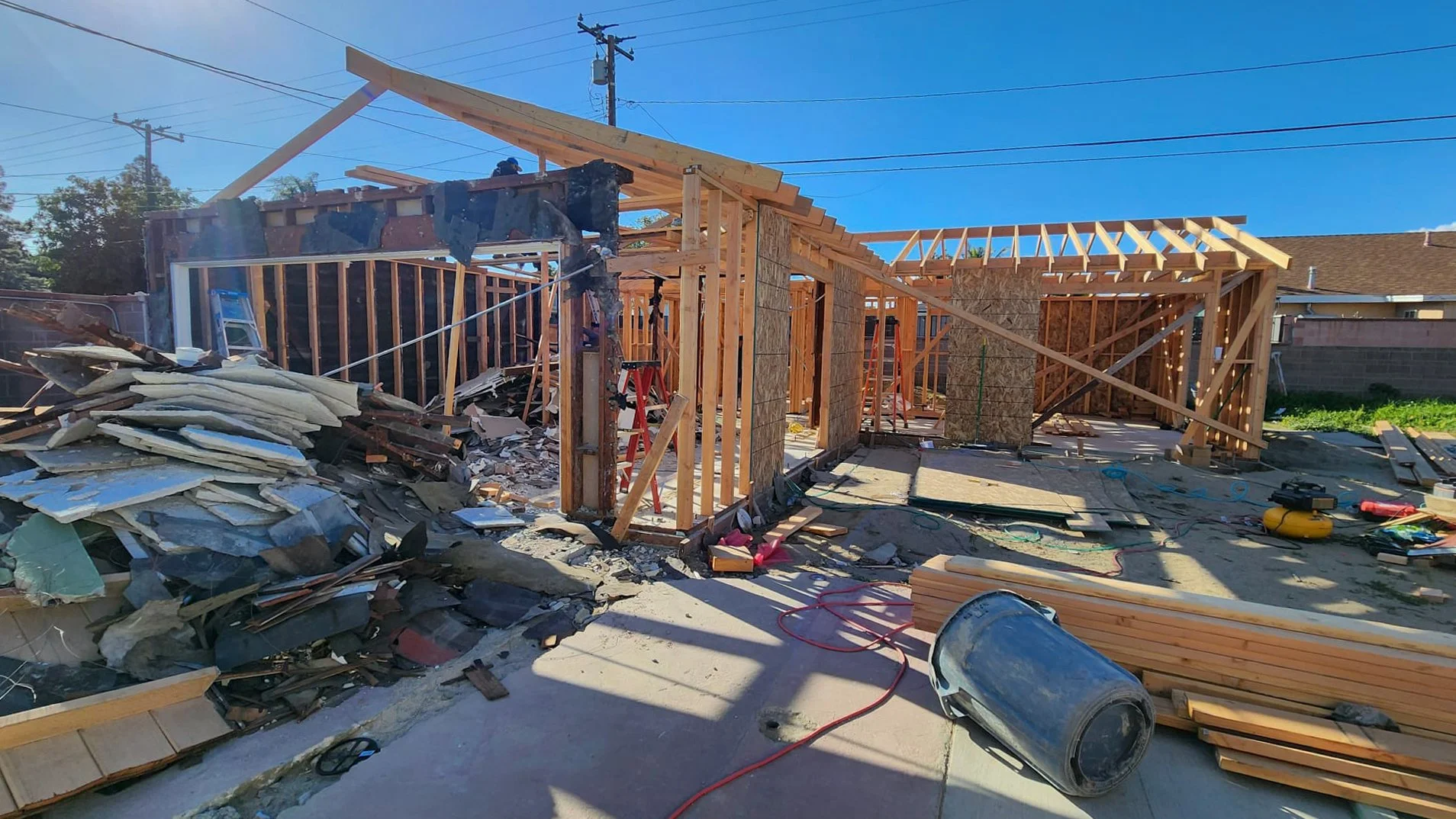 Construction site with wooden framing for a house in progress, debris, construction tools, and materials scattered around.