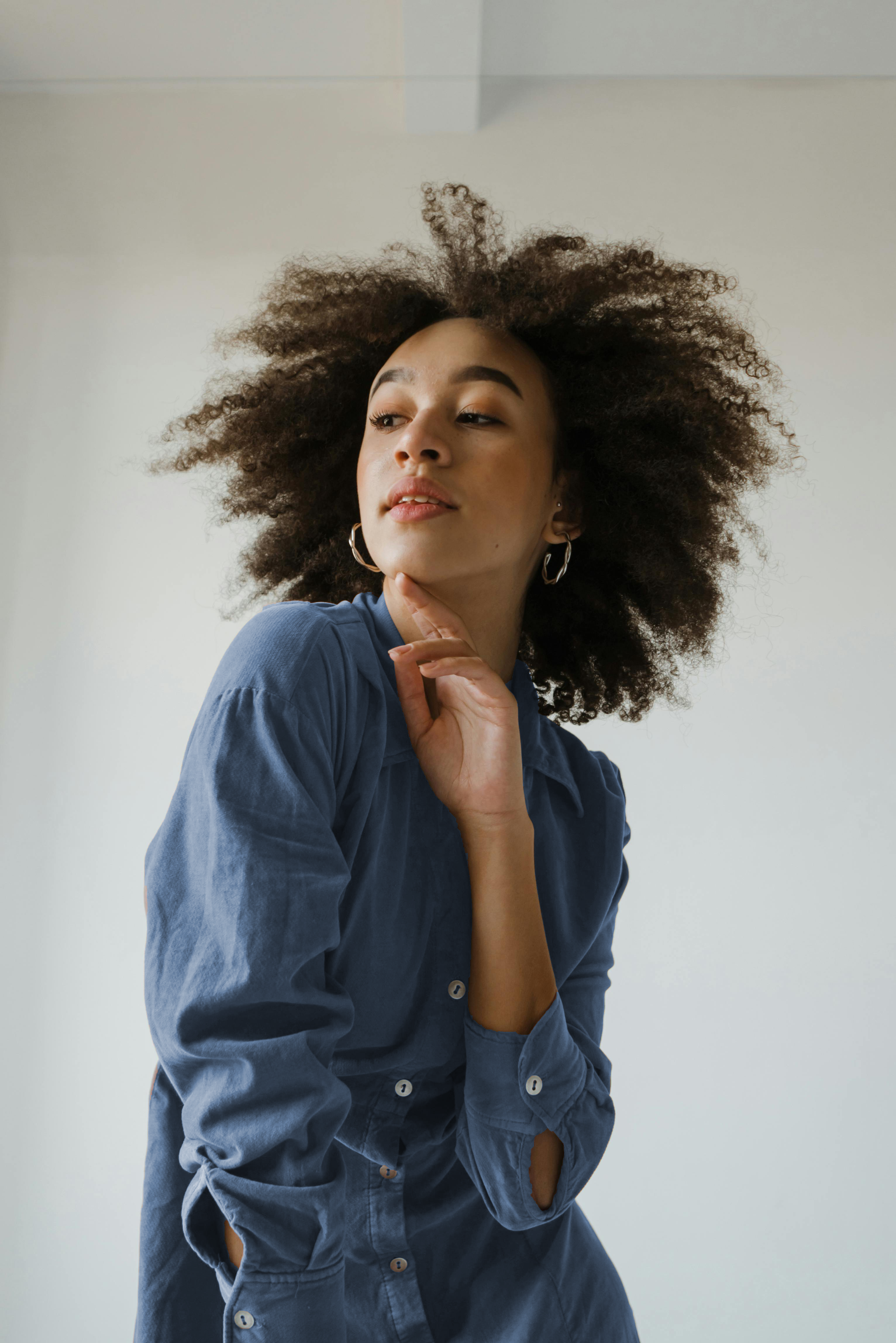 A young woman with curly hair, wearing earrings and a blue shirt, posed against a neutral background.