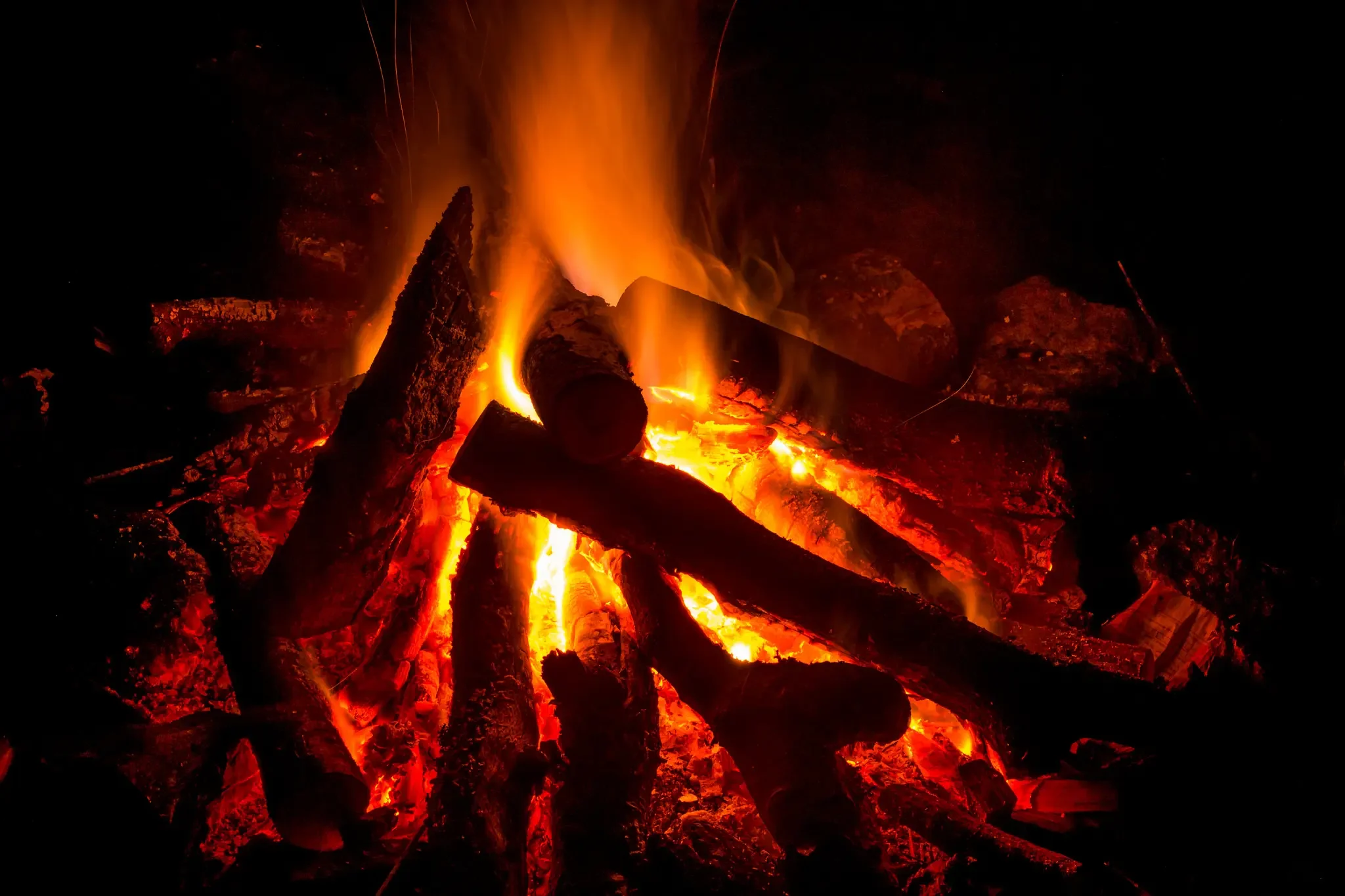 Fires burning brightly with glowing embers and tall flames, charred logs, and ash, at night.
