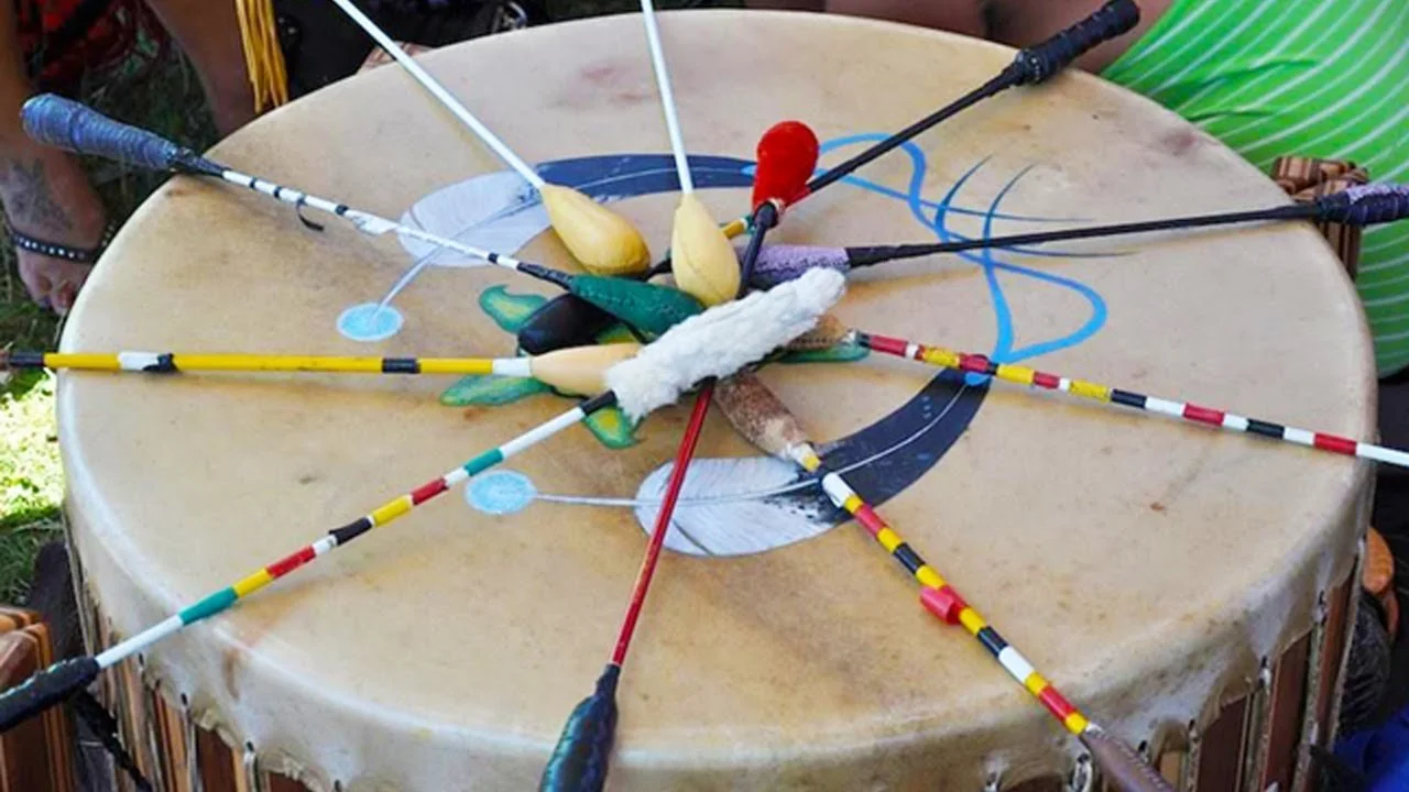 A drum with multiple colorful arrows stuck into it, some with feathers, arranged in a circular pattern.