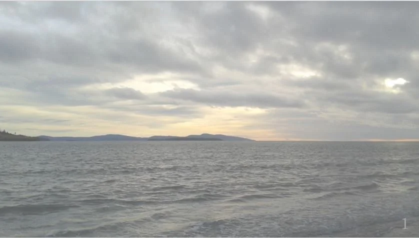 Overcast sky with a calm ocean and distant land in the background.