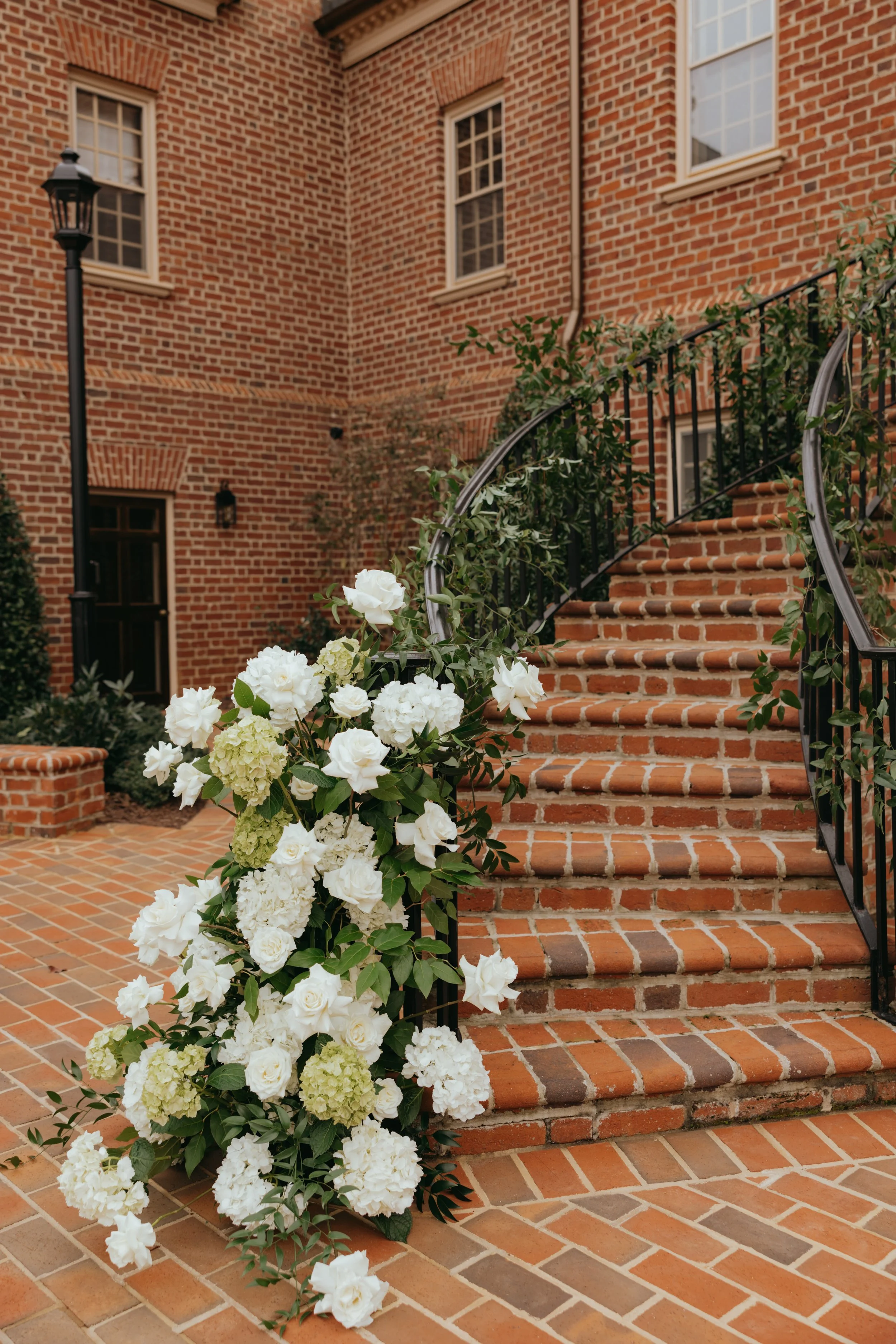 Brick staircase decorated with white and light green floral arrangement, set against brick building with windows and a lamppost.
