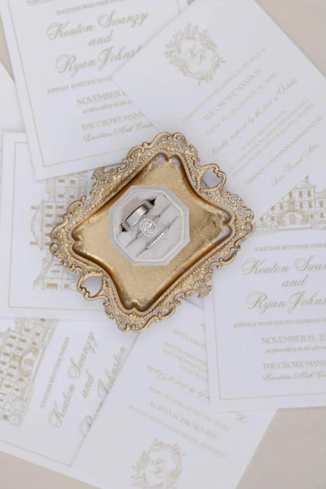 A decorative jewelry box containing engagement and wedding rings, placed on wedding invitations with elegant gold and white design.
