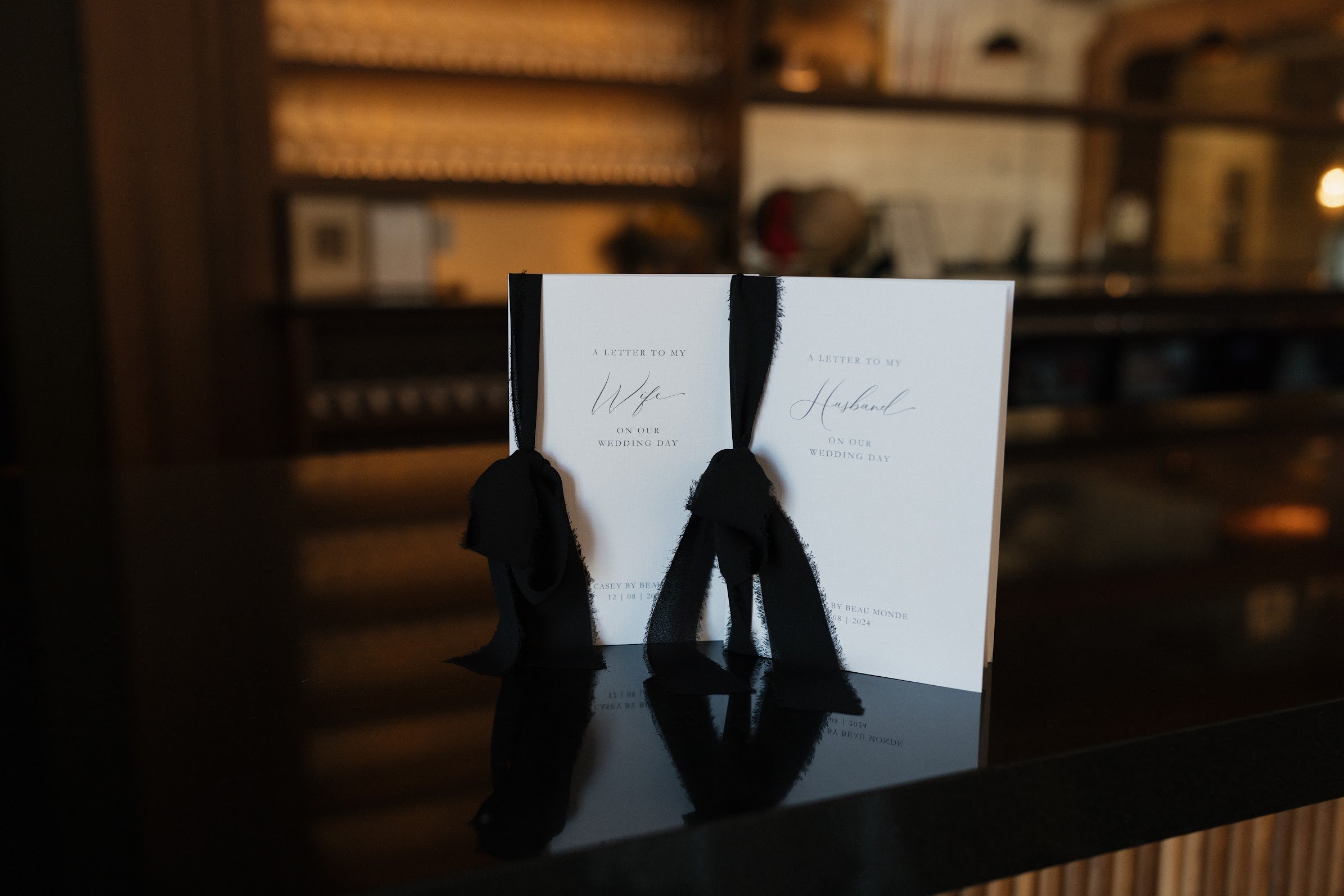 Wedding programs or invitations with black ribbon bows on a dark table, with a blurred wooden background.
