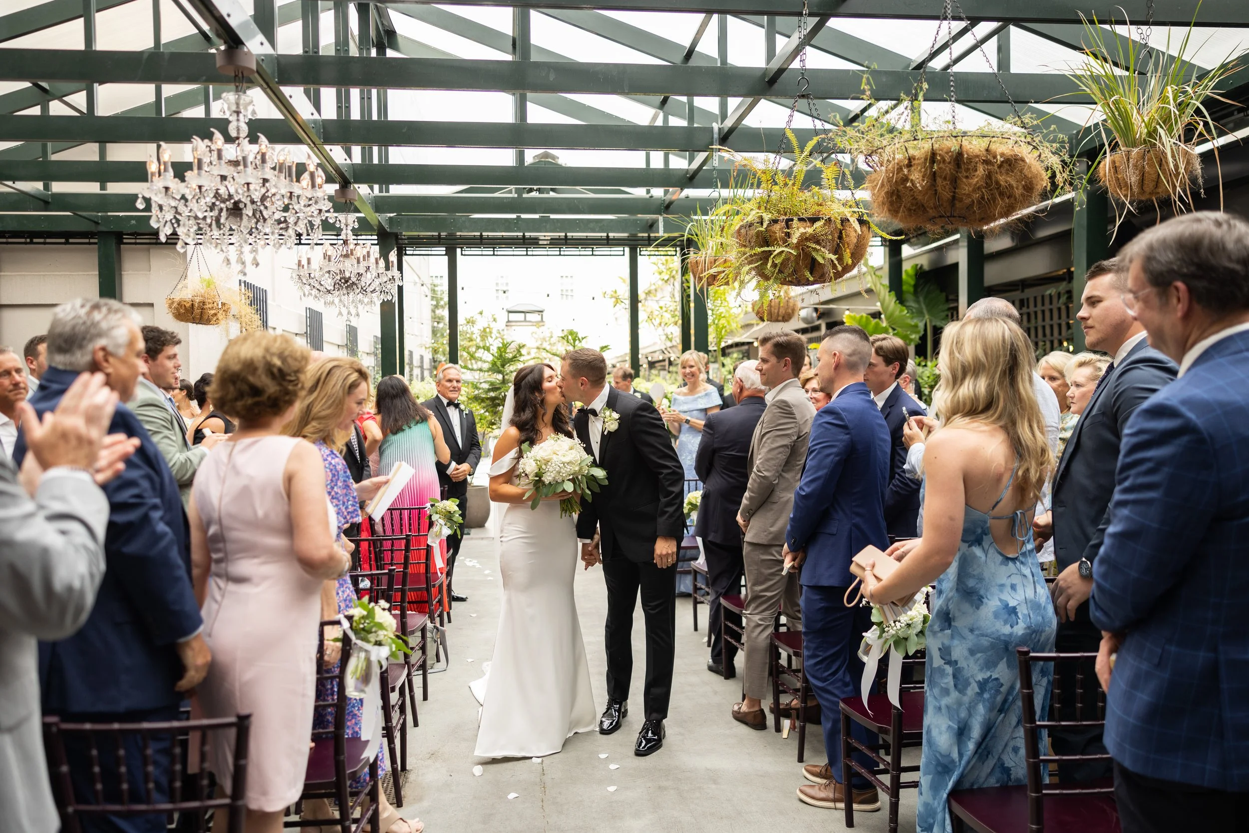 Bride and groom kissing during their wedding ceremony in an outdoor venue with guests seated on both sides.