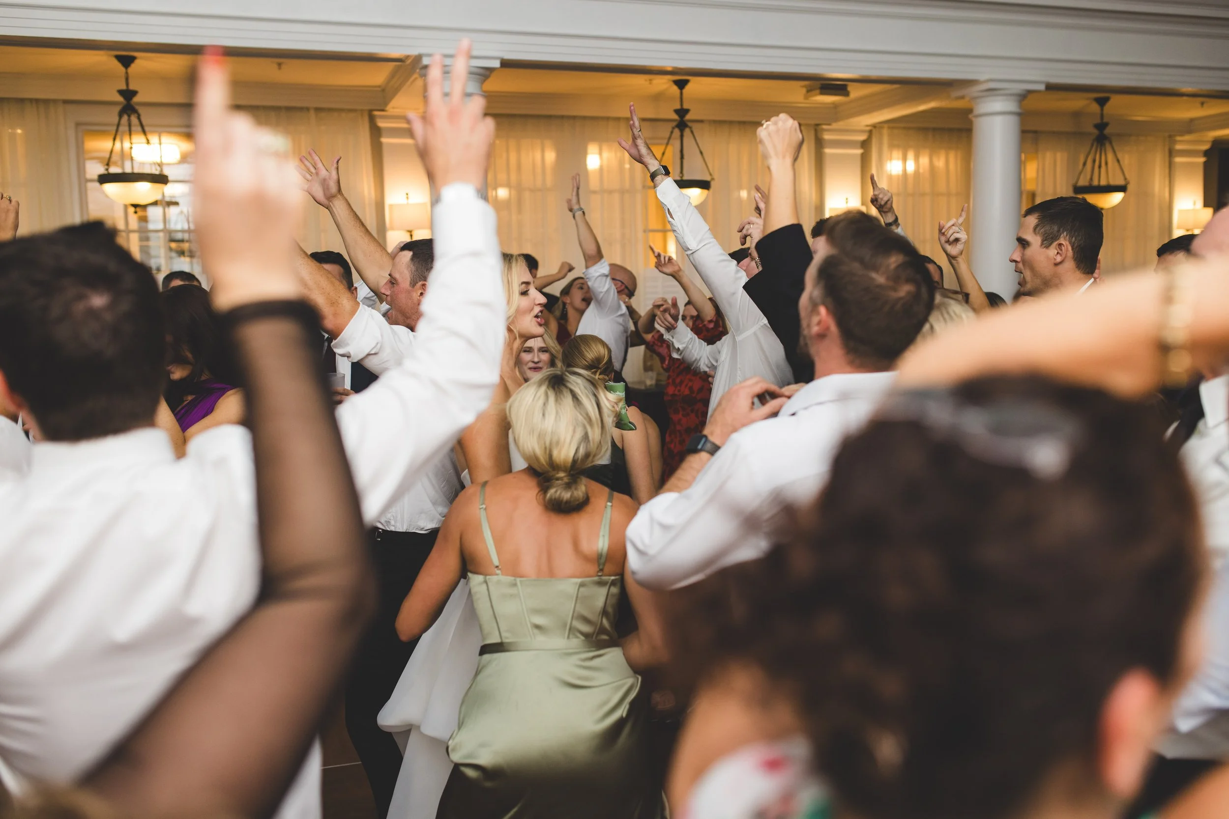 People dancing and celebrating at a wedding reception with hands raised in the air.