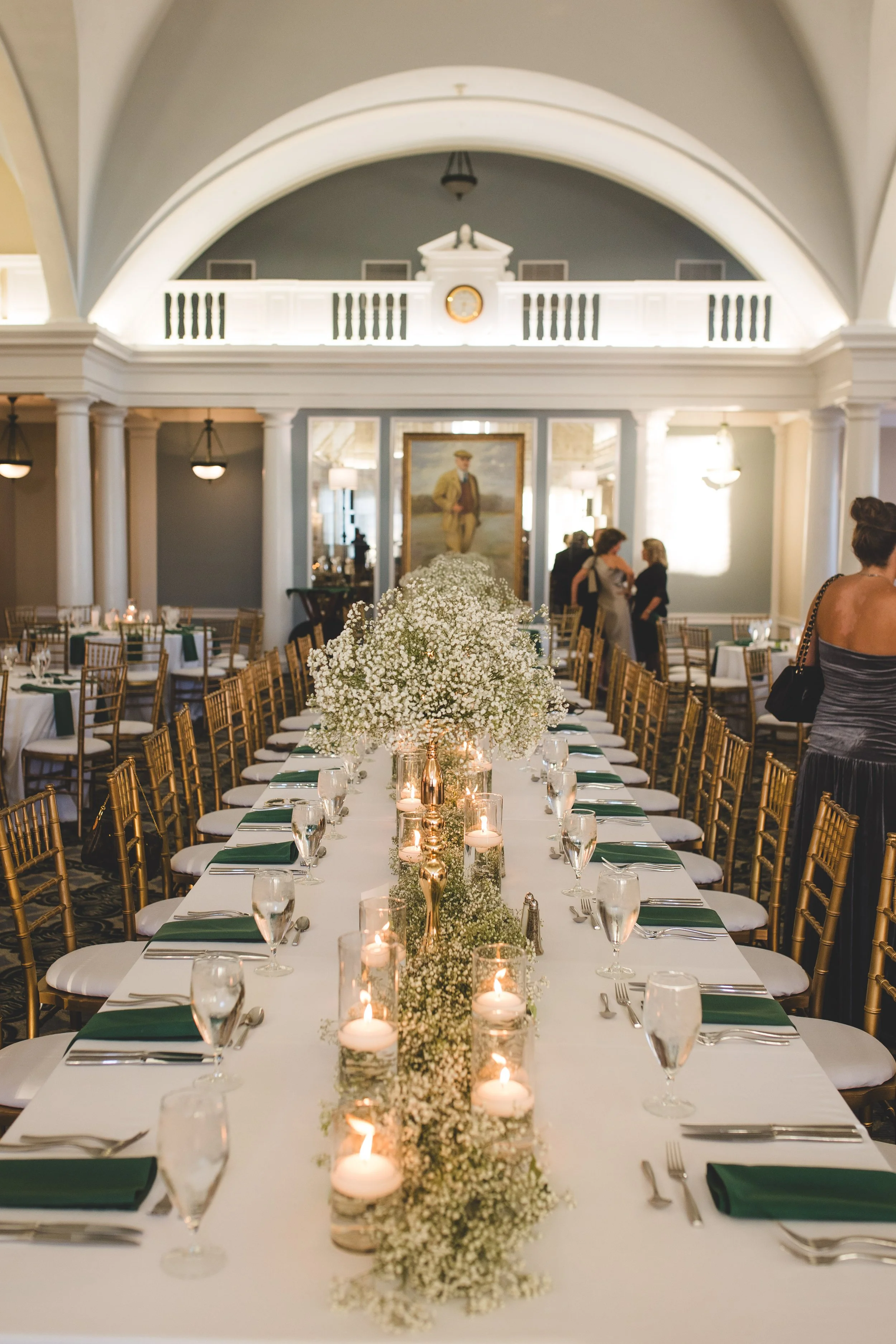 Elegant wedding reception with a long dining table decorated with white flowers and candles, set in a grand hall with high vaulted ceilings and classical architecture.