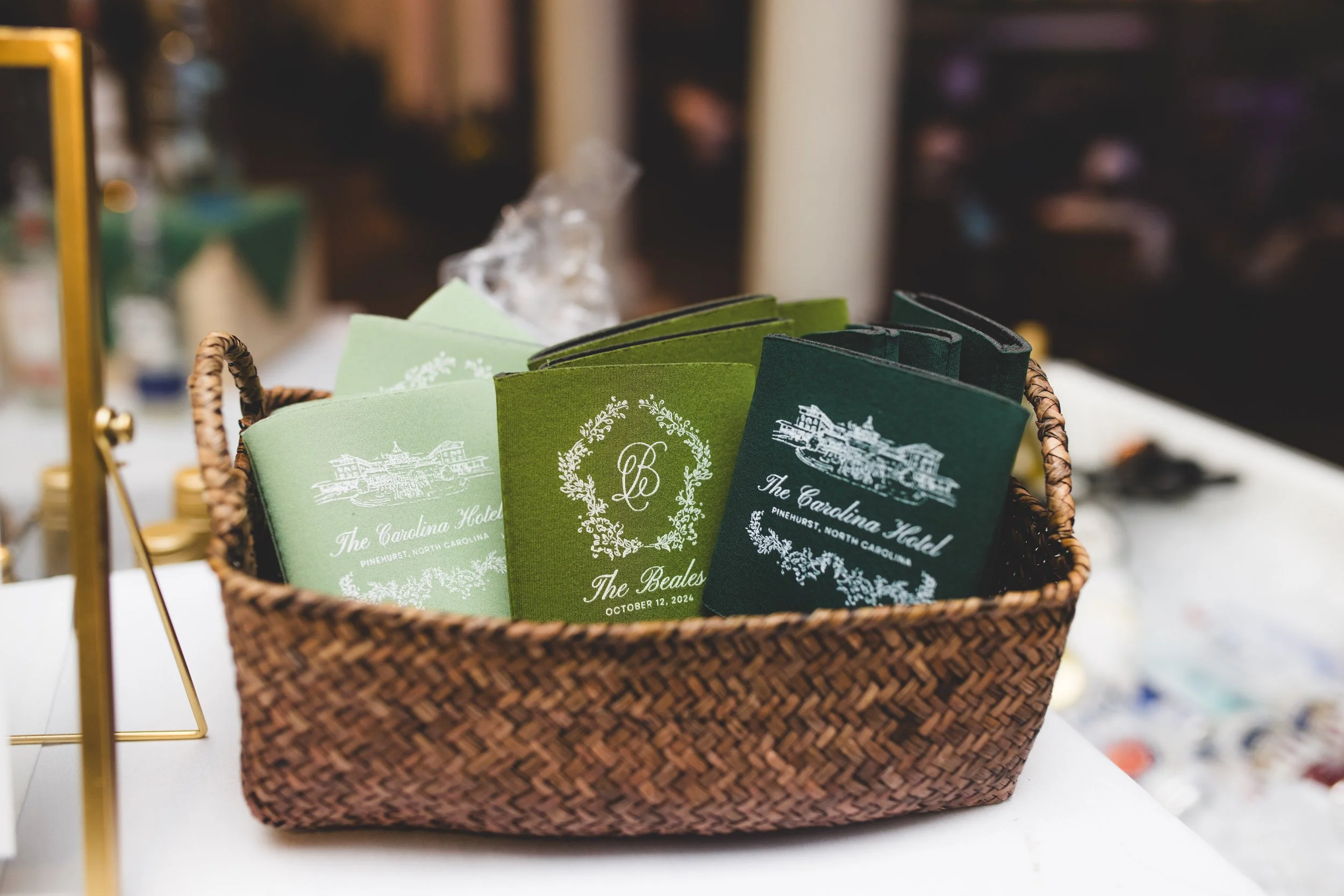 A woven basket containing green and dark green wedding programs for The Carolina Hotel in Pinehurst, North Carolina.
