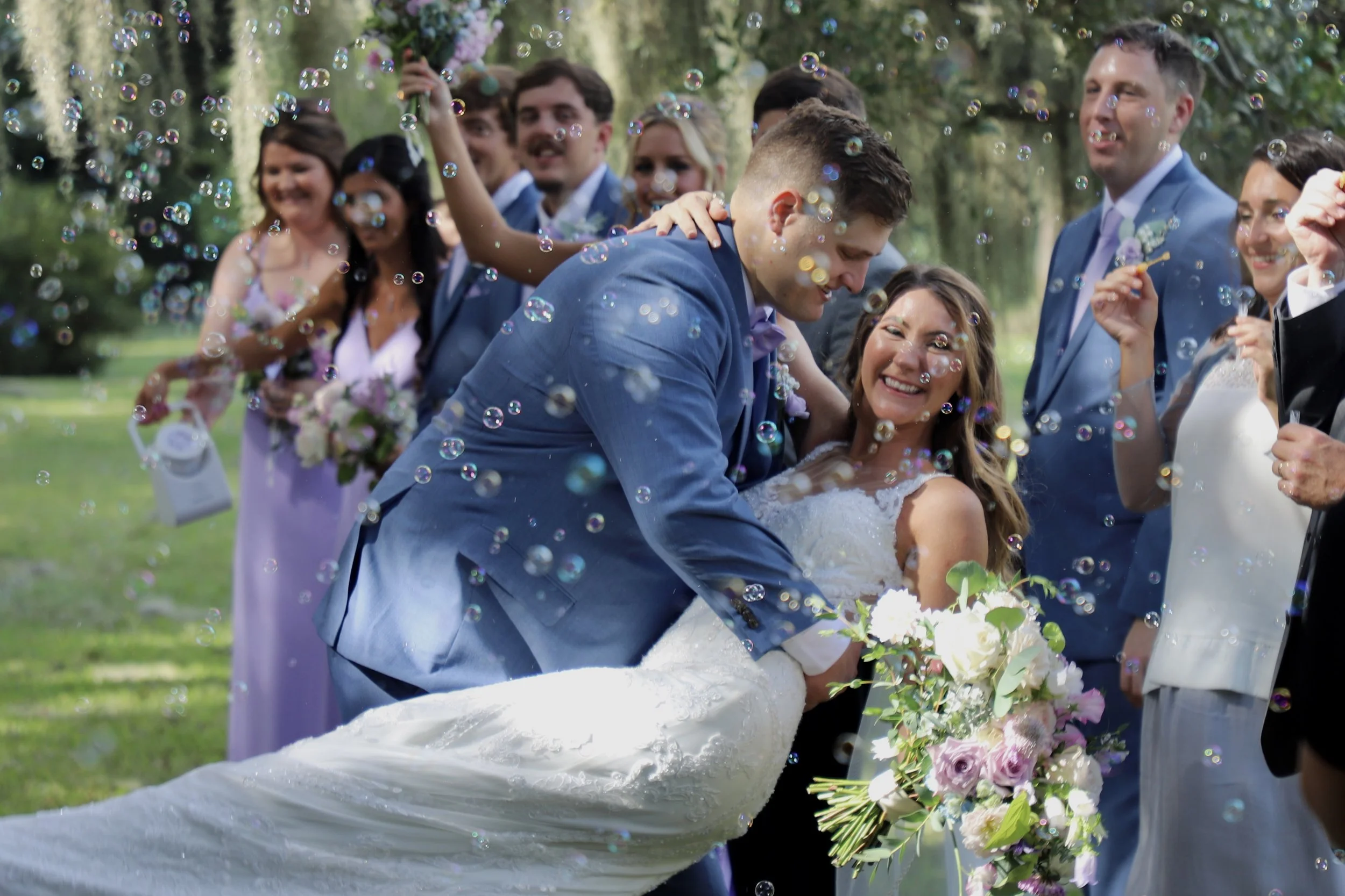 A joyful bride and groom surrounded by friends and family outdoors, with bubbles floating in the air, as they celebrate their wedding.