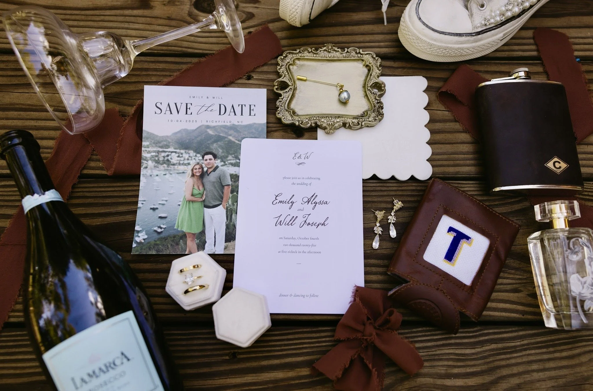 Wedding invitation with photos, jewelry, a perfume bottle, wine, glasses, and accessories arranged on a wooden surface.